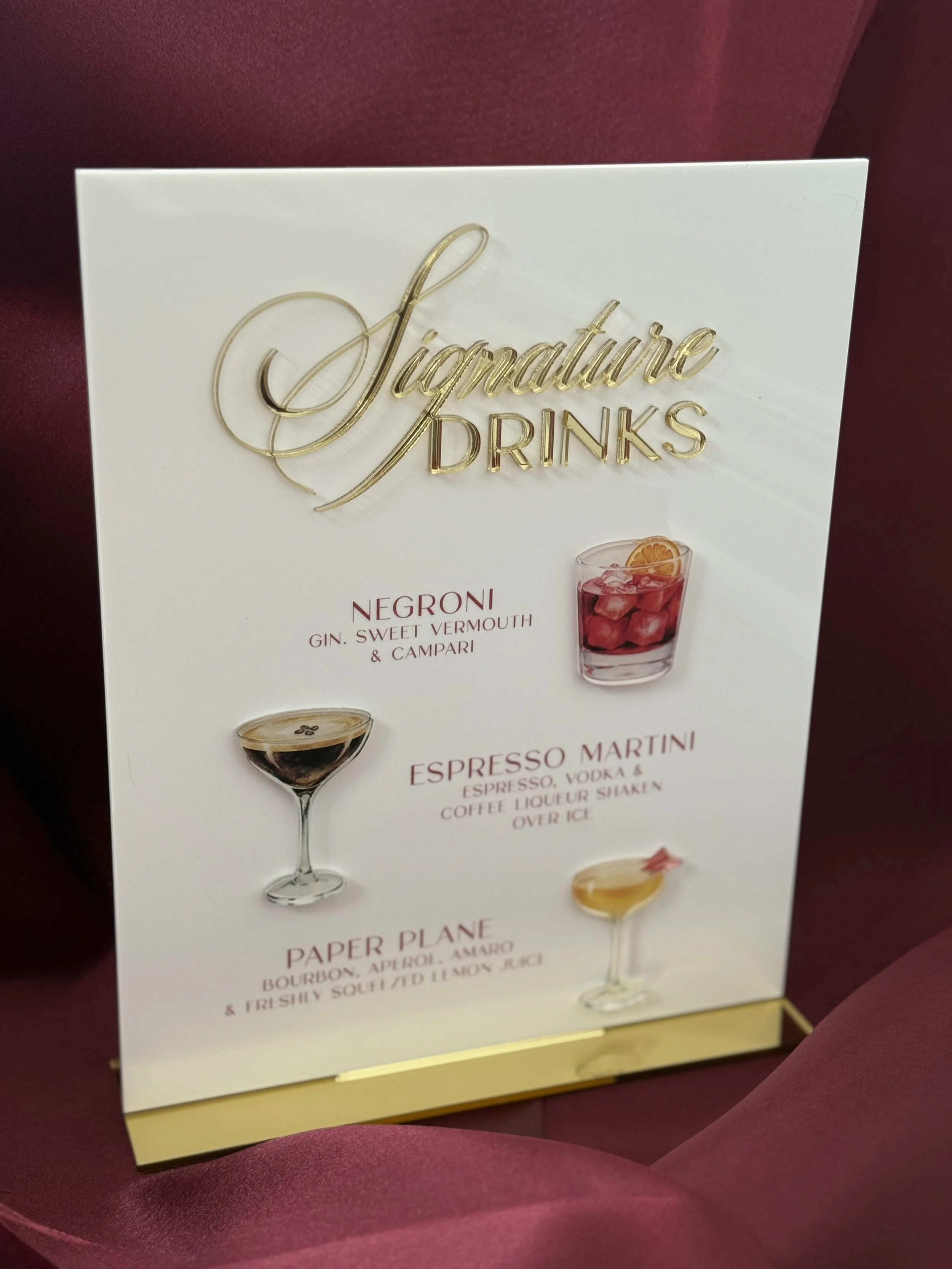 Menu sign with gold and red lettering offering three signature drinks: Negroni, Espresso Martini, and Paper Plane, each with a description and images of the drinks.