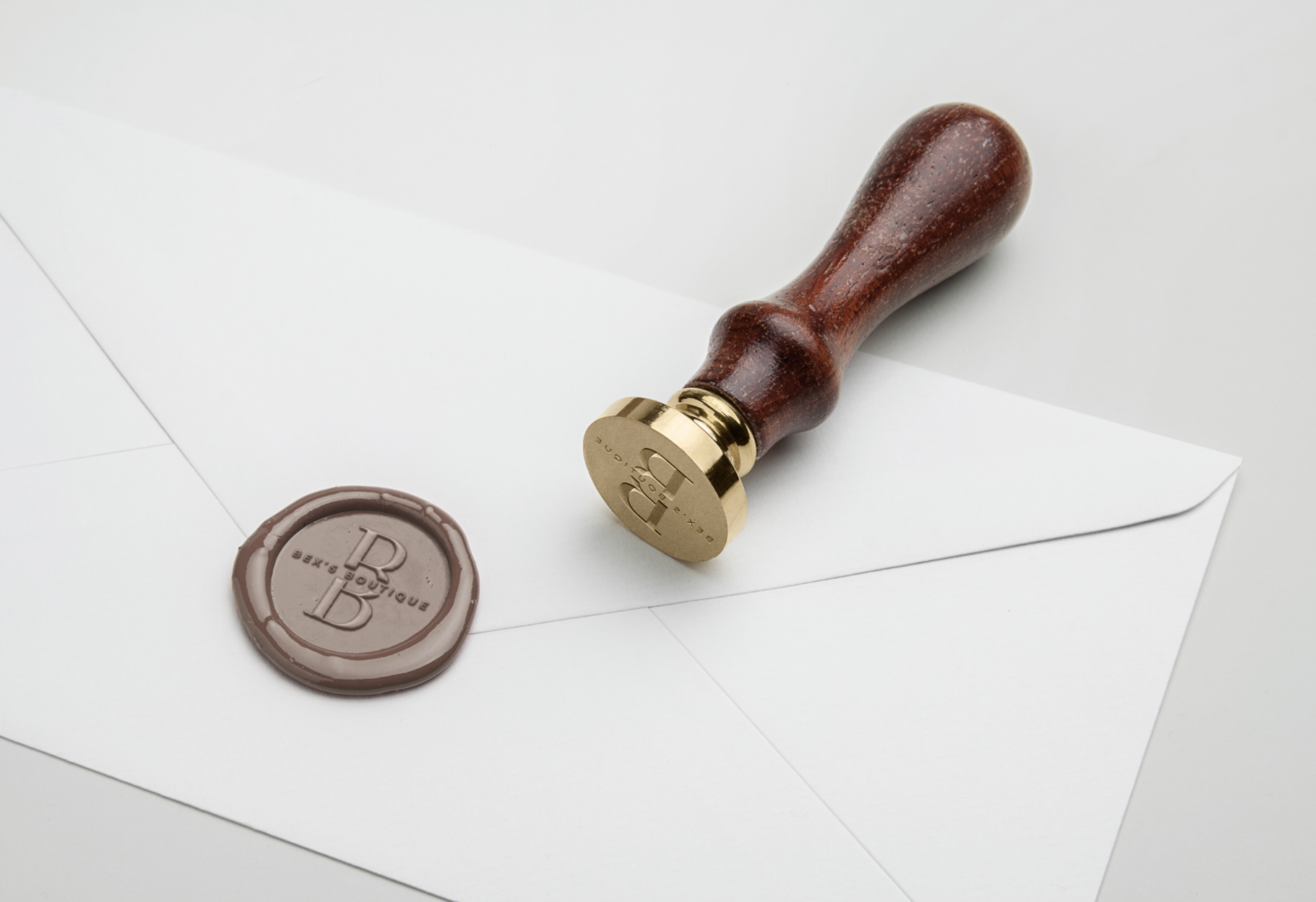 A wooden-handled wax seal stamp resting on a white envelope, with a brown wax seal stamped with the letter 'B' nearby.