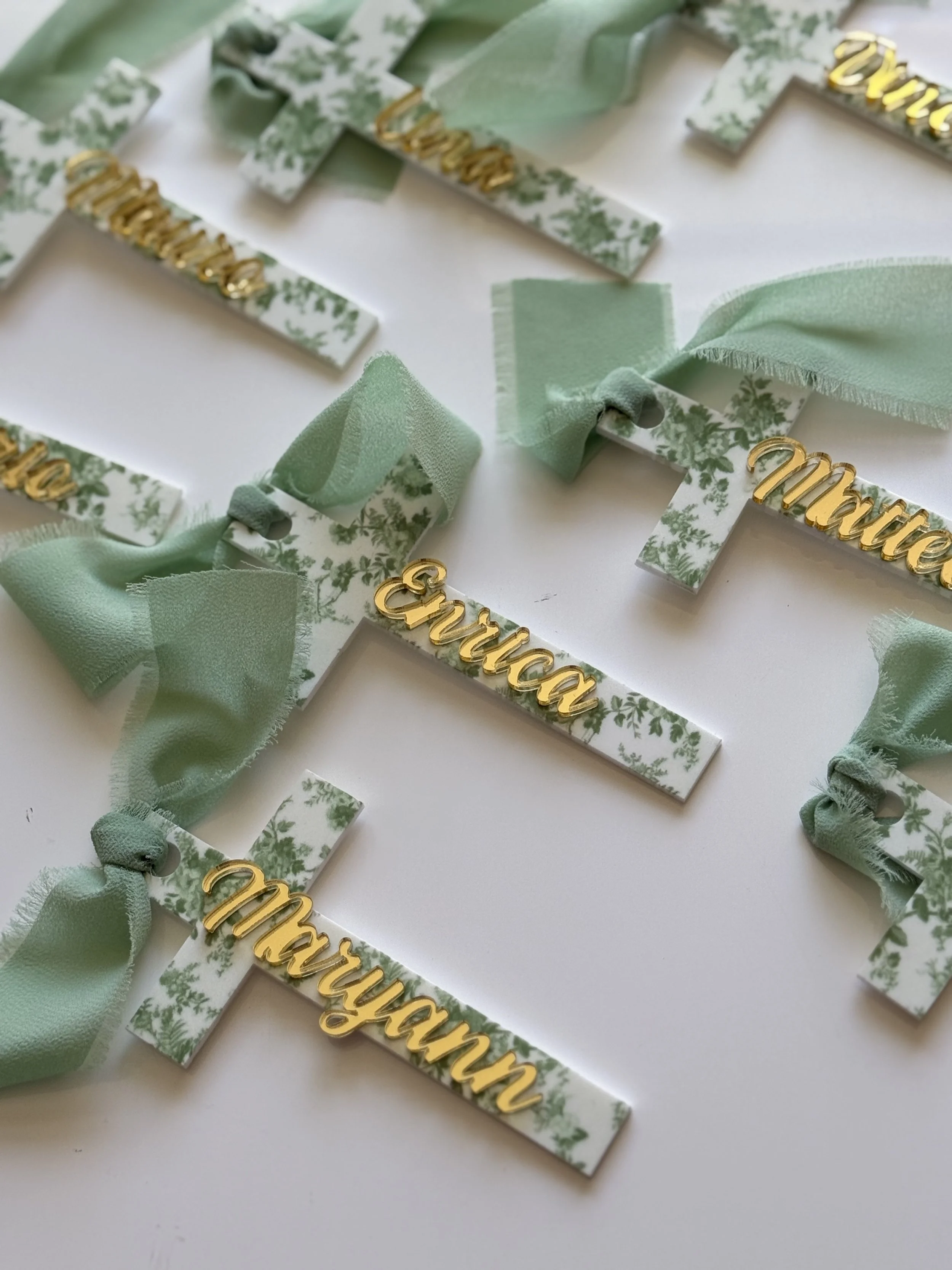 Decorative crosses with green floral pattern, gold cursive names, and green ribbons.