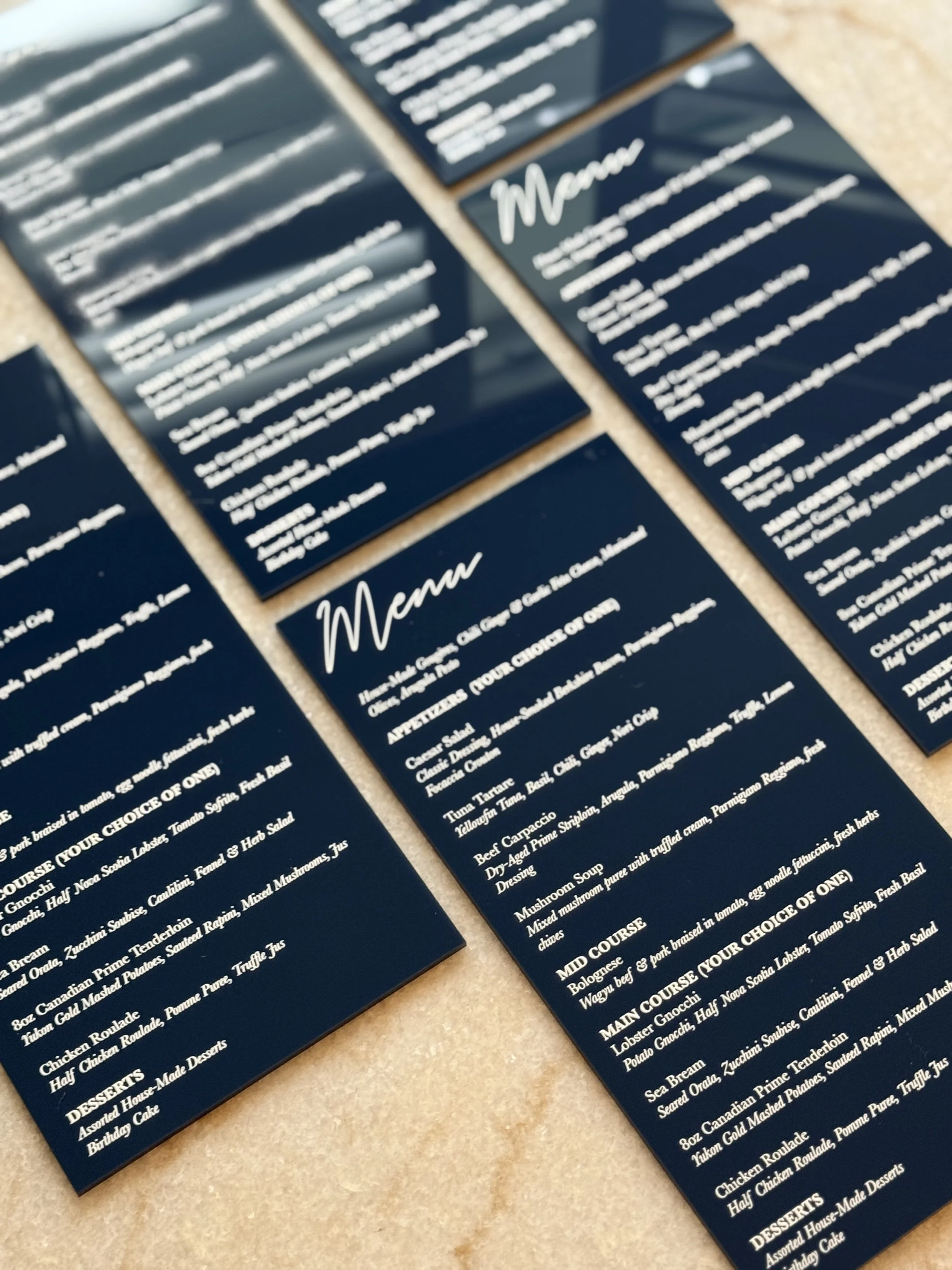 Close-up photo of navy blue printed menus with white cursive headings on a beige table.