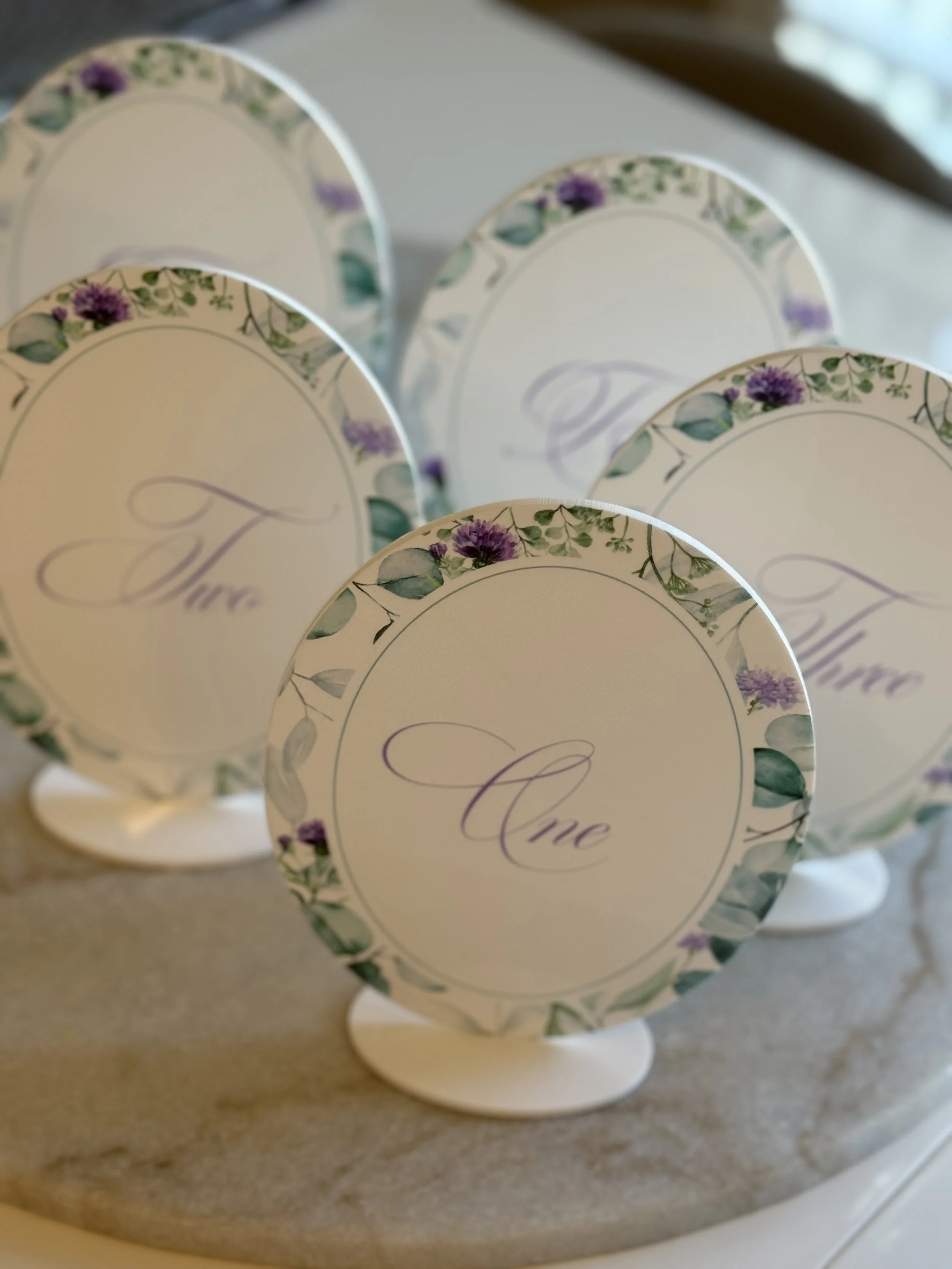 Elegant place cards with a floral border and the name 'Anne' written in script, set on a marble surface.
