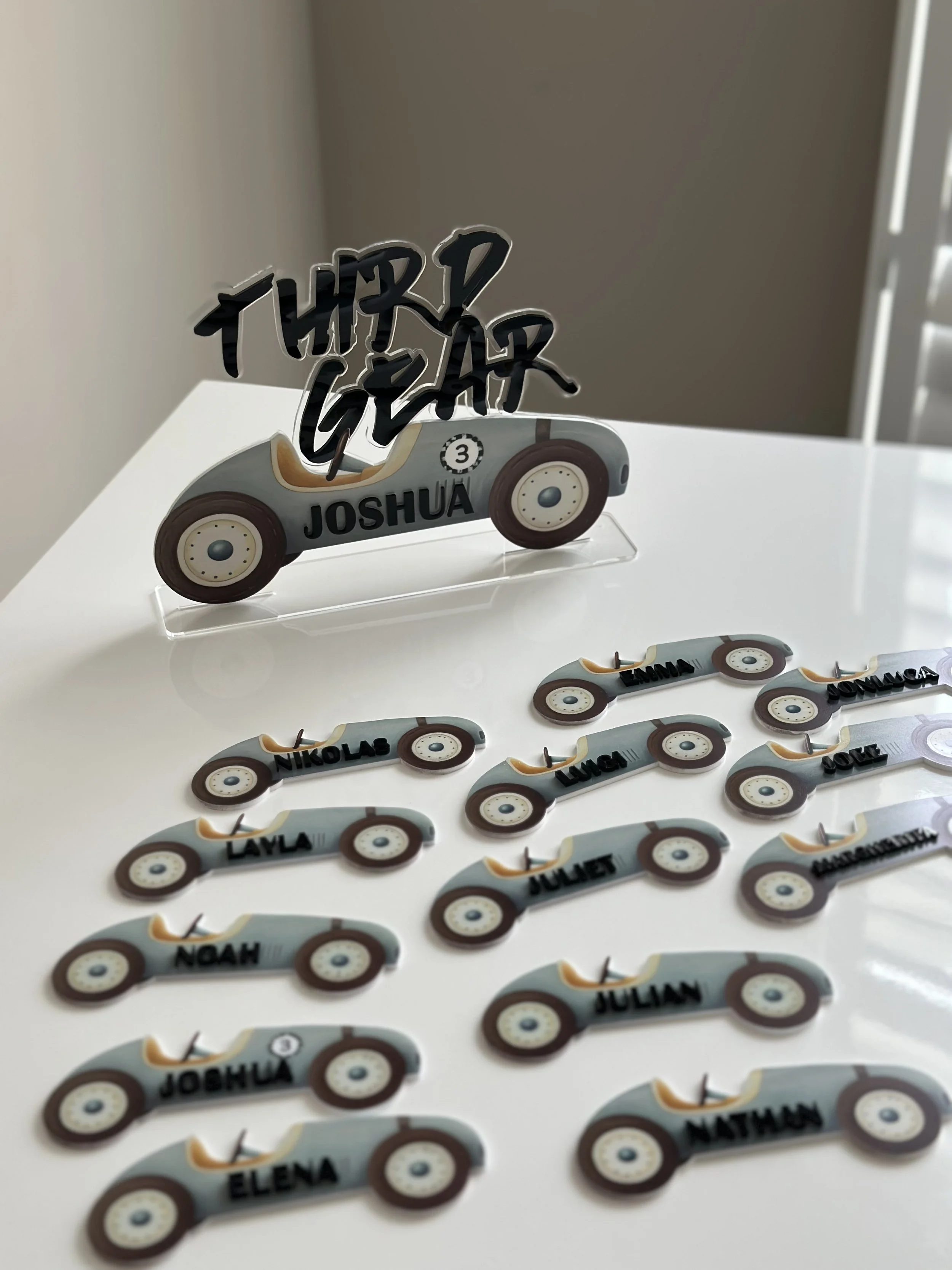 Toy race cars with names and a decorative sign reading 'THINK GEAR' on a white table.