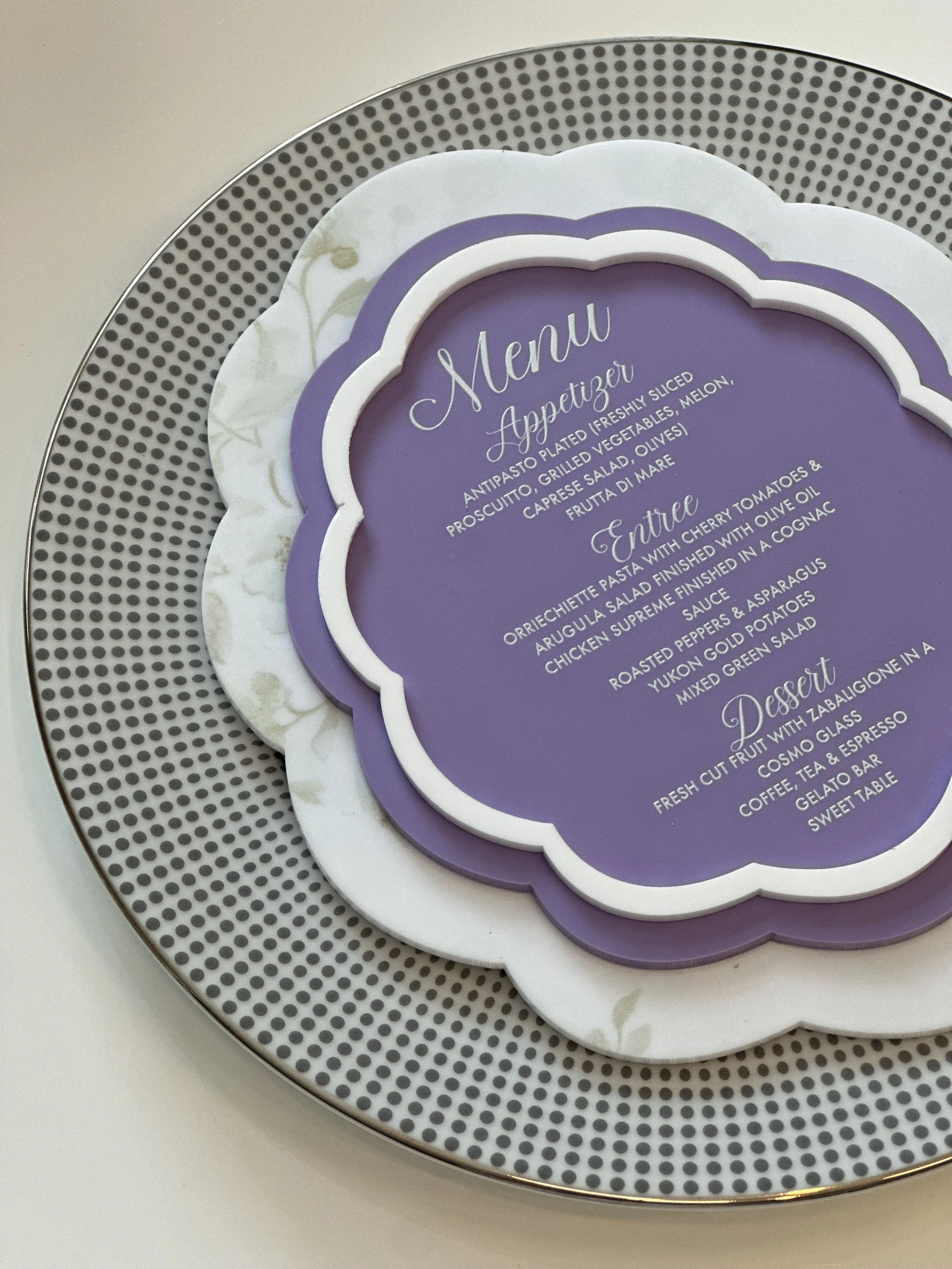 Elegant restaurant menu on a purple and white scalloped paper, placed on a decorative black and white dotted plate.