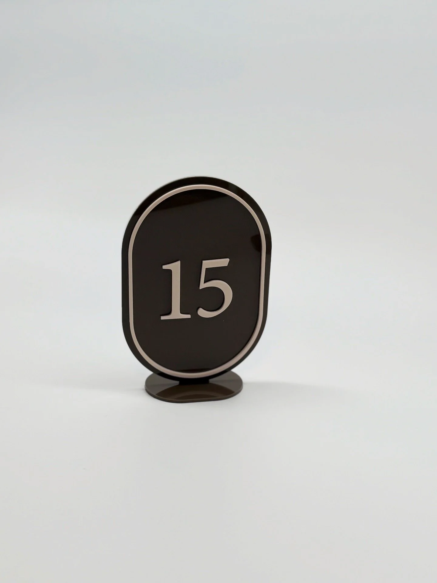 A black oval table number sign displaying the number 15, standing on a small circular base against a plain white background.