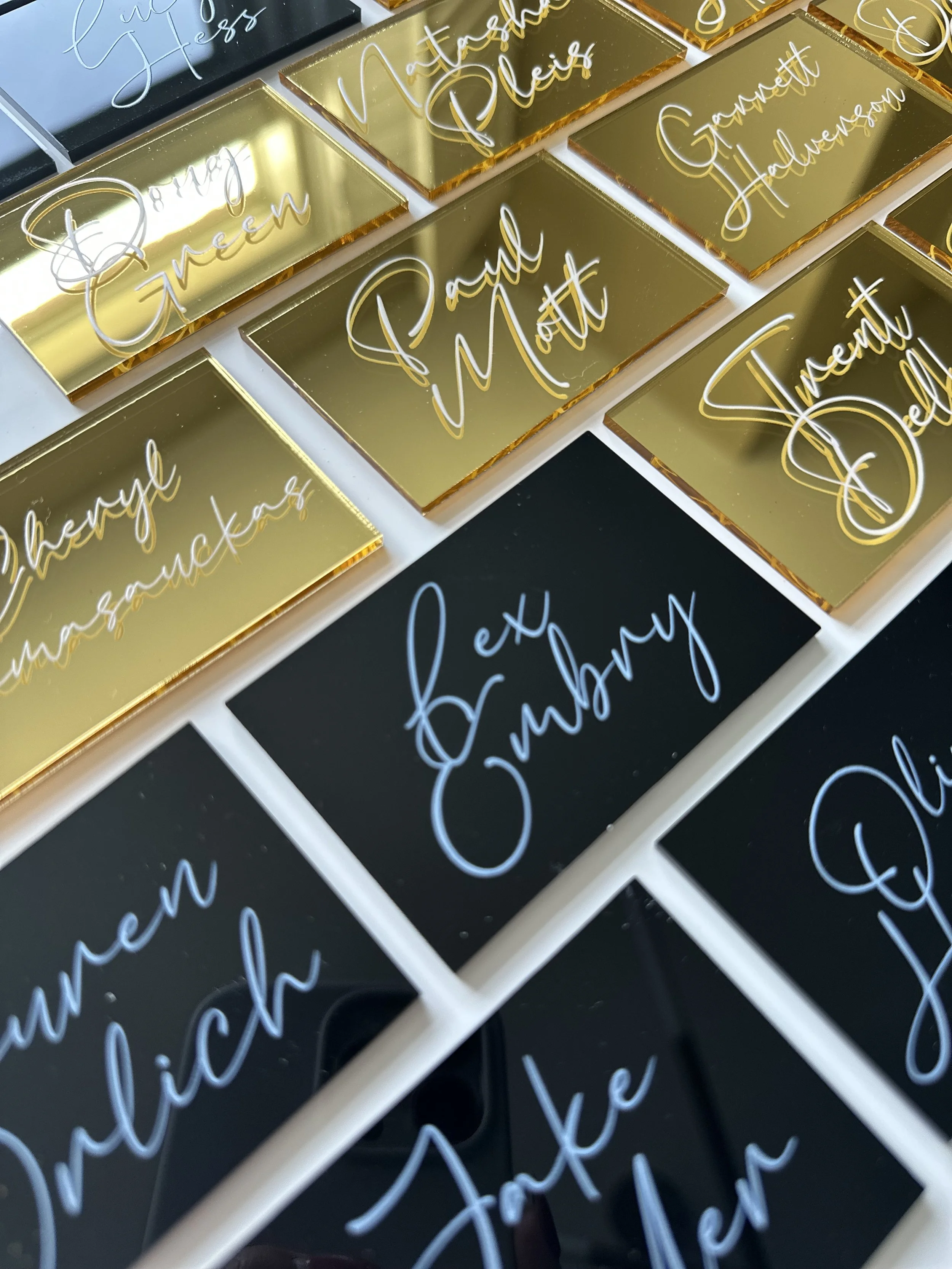 Collection of decorative signs with various phrases such as "Thank you," "Meeting Notes," "Garnett Showeron," and "Eat Embark," written in elegant cursive on shiny gold, black, and white backgrounds.