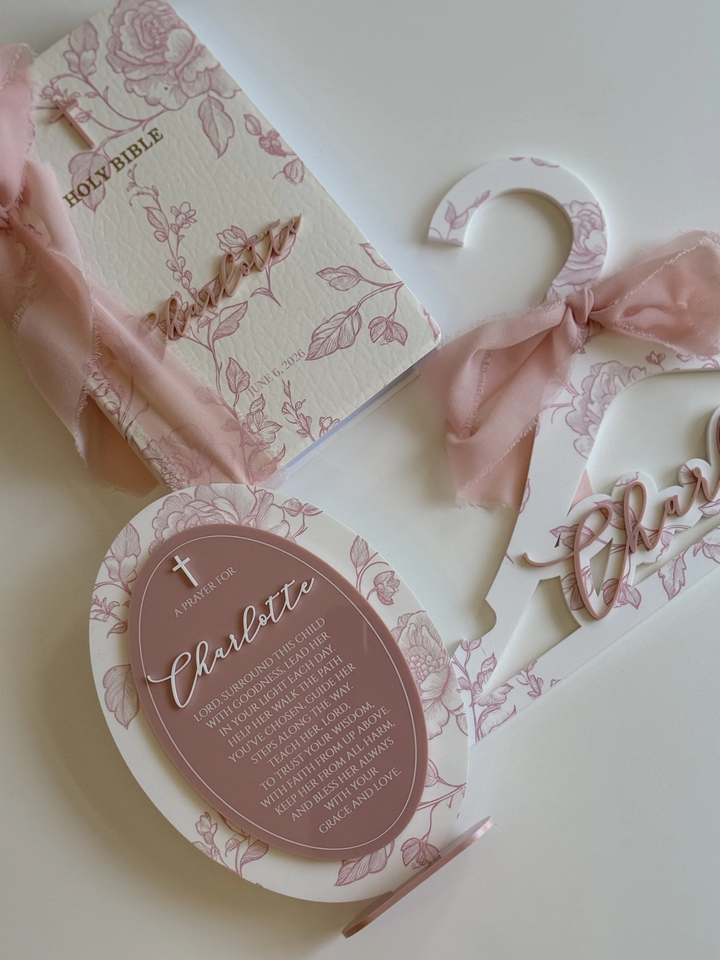 A decorative card with floral designs and the name Charlotte, featuring a Bible verse and a pink ribbon tied in a bow across the card.