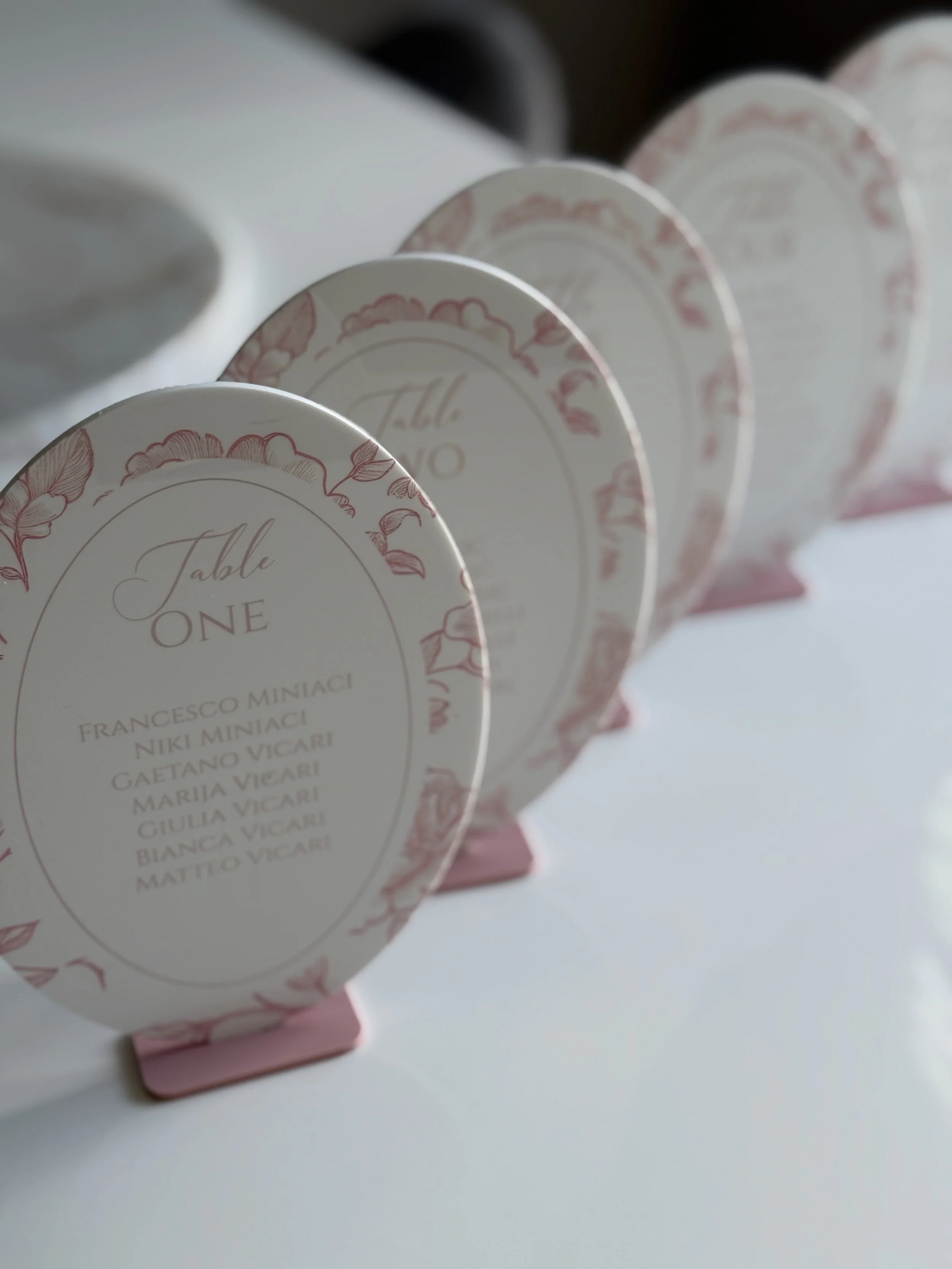 Decorative table place cards with floral border, listing names of guests and table number.