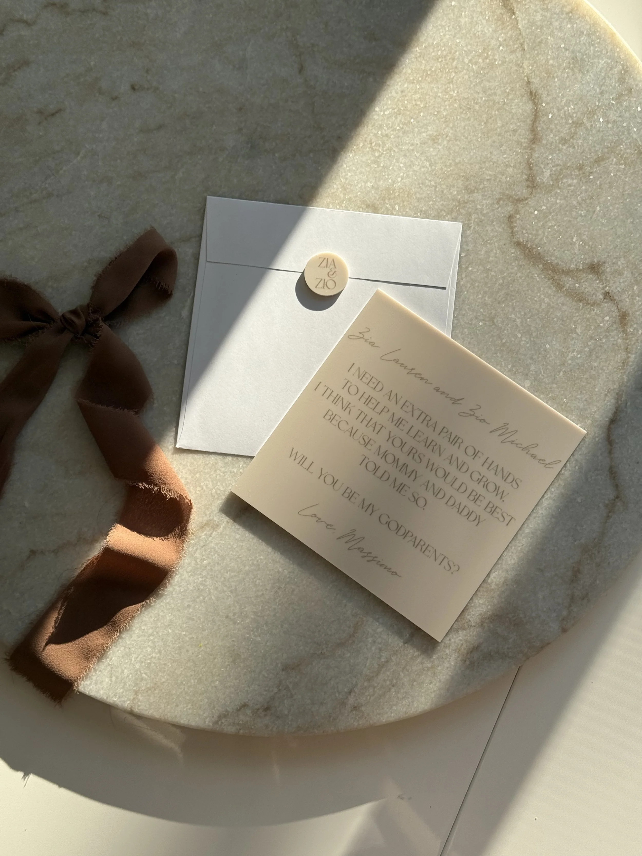 A handwritten note and an envelope with a wax seal are placed on a light-colored surface with sunlight casting shadows. The note is addressed to Zia Lauren and Zia Michael, with a romantic message signed by Love, Massima.