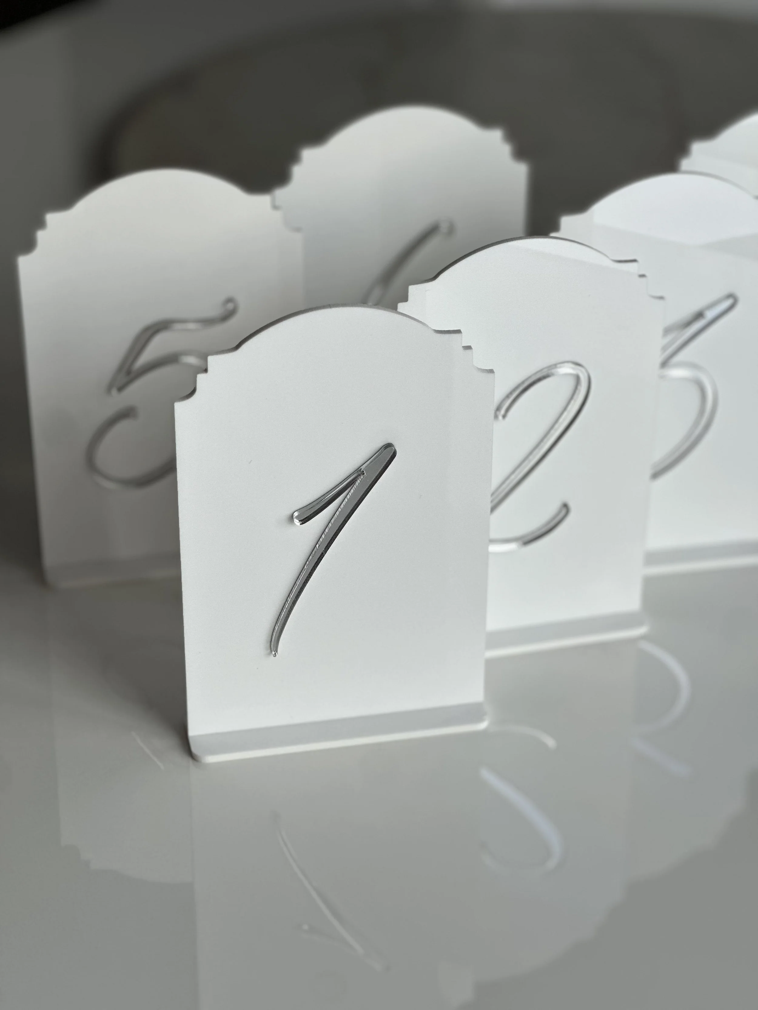 Number seven on a white card with a metallic hook, part of a series with other numbers, reflected on a smooth surface.