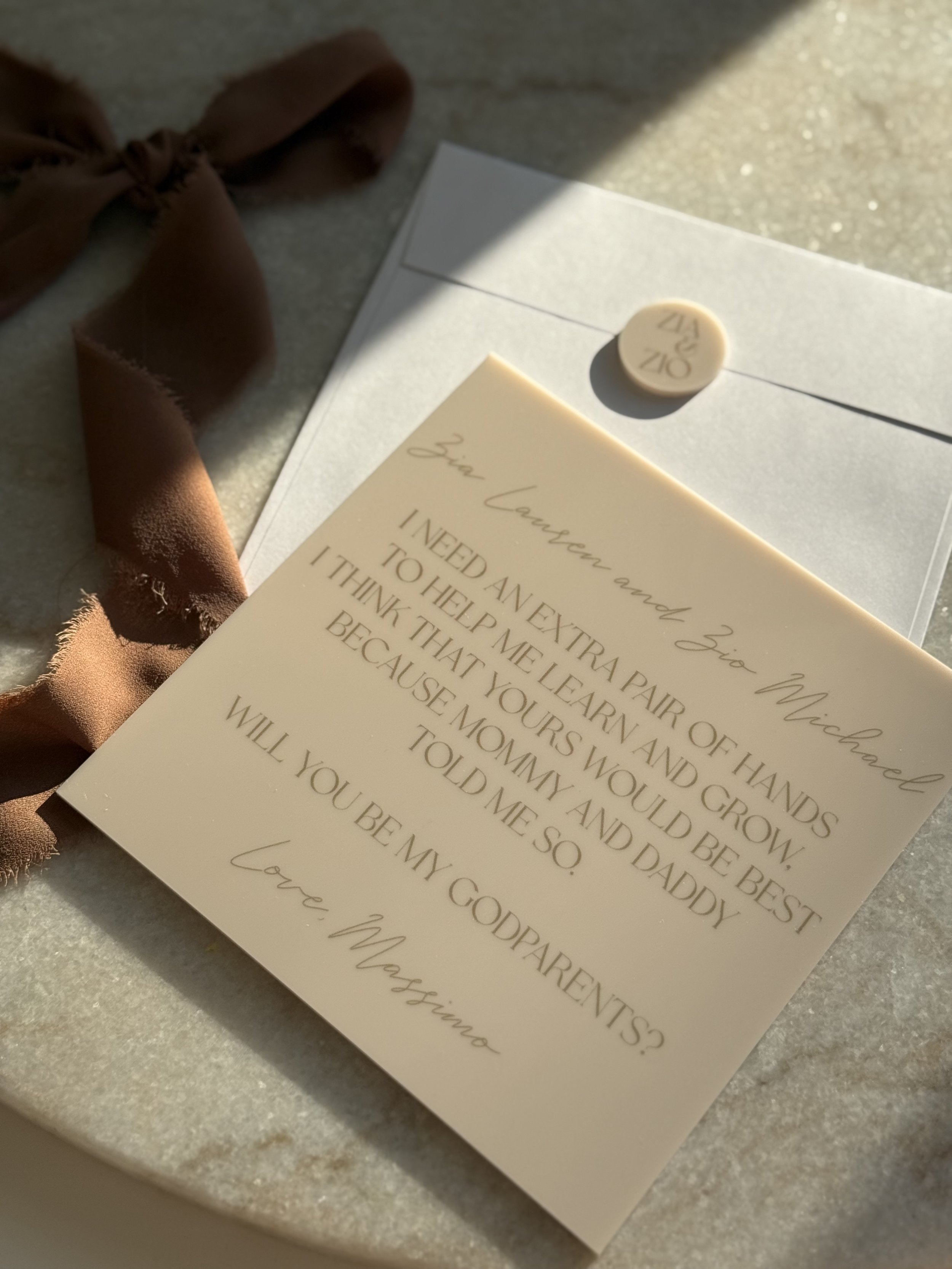 A handwritten note with a poem or message, placed on a white envelope with a round sticker, and a brown ribbon on a surface, illuminated by sunlight.
