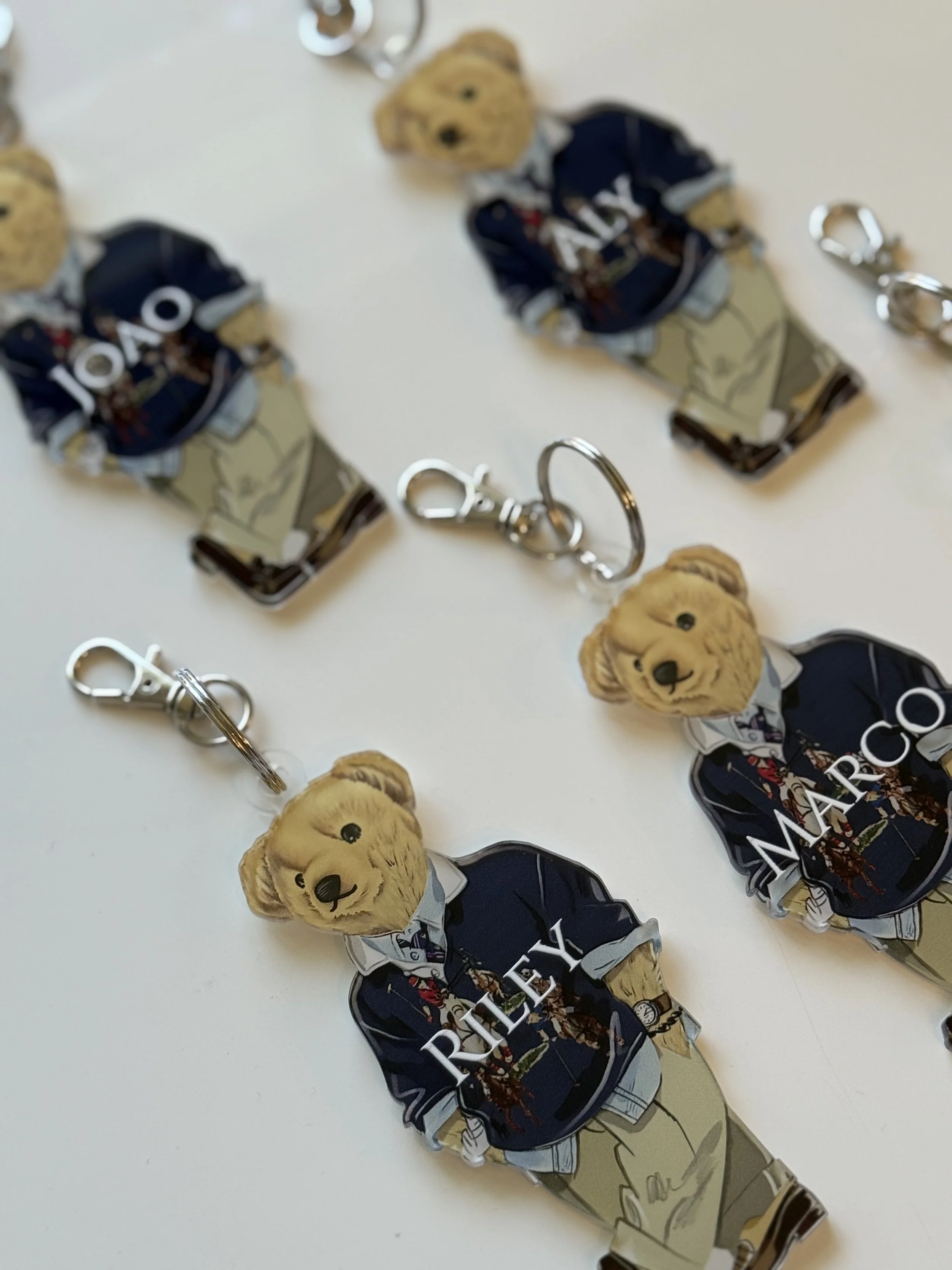 Keychains featuring teddy bears dressed in Ralph Lauren polo shirts and khaki pants with the names 'REIY' and 'MARY C.' displayed.