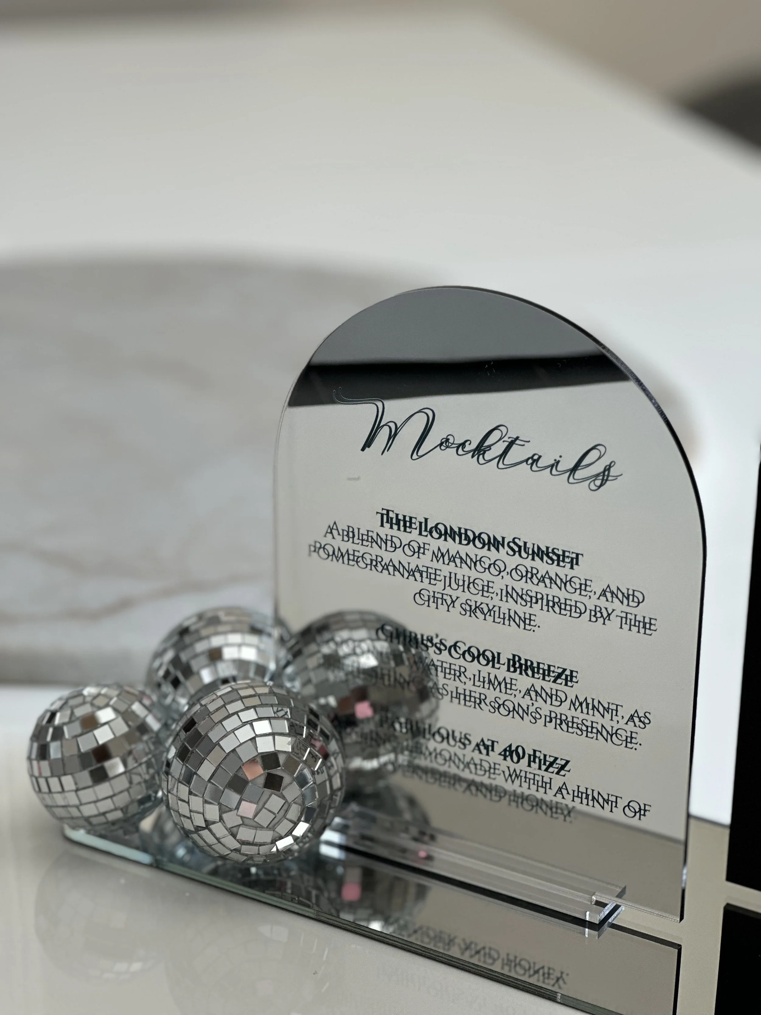 Mirror with cocktail menu and small disco balls on a reflective surface.