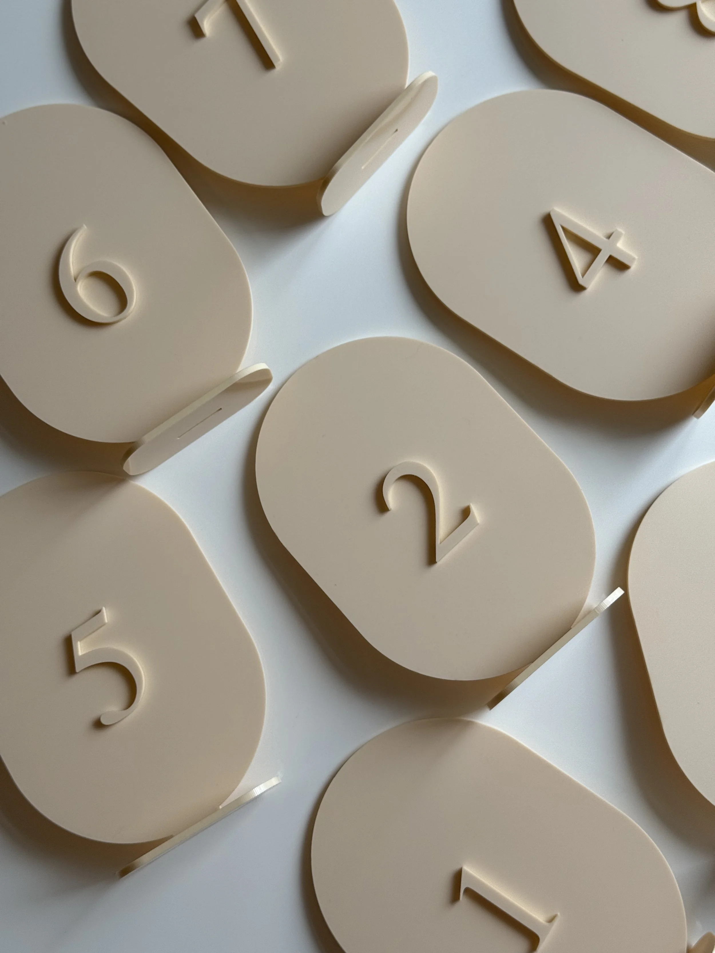 Close-up of beige oval-shaped number tags with embossed numbers 1, 2, 4, 5, and 6 scattered on a white surface.