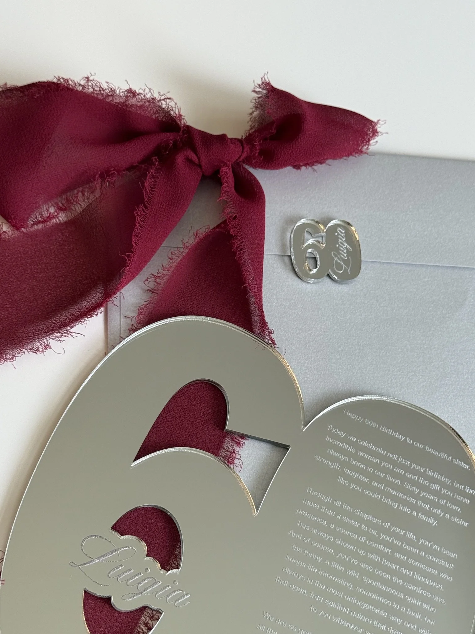 Close-up of a greeting card with a large cutout of the number 60 in gold with silver accents, a red ribbon tied into a bow, and an embedded message celebrating a 60th birthday.