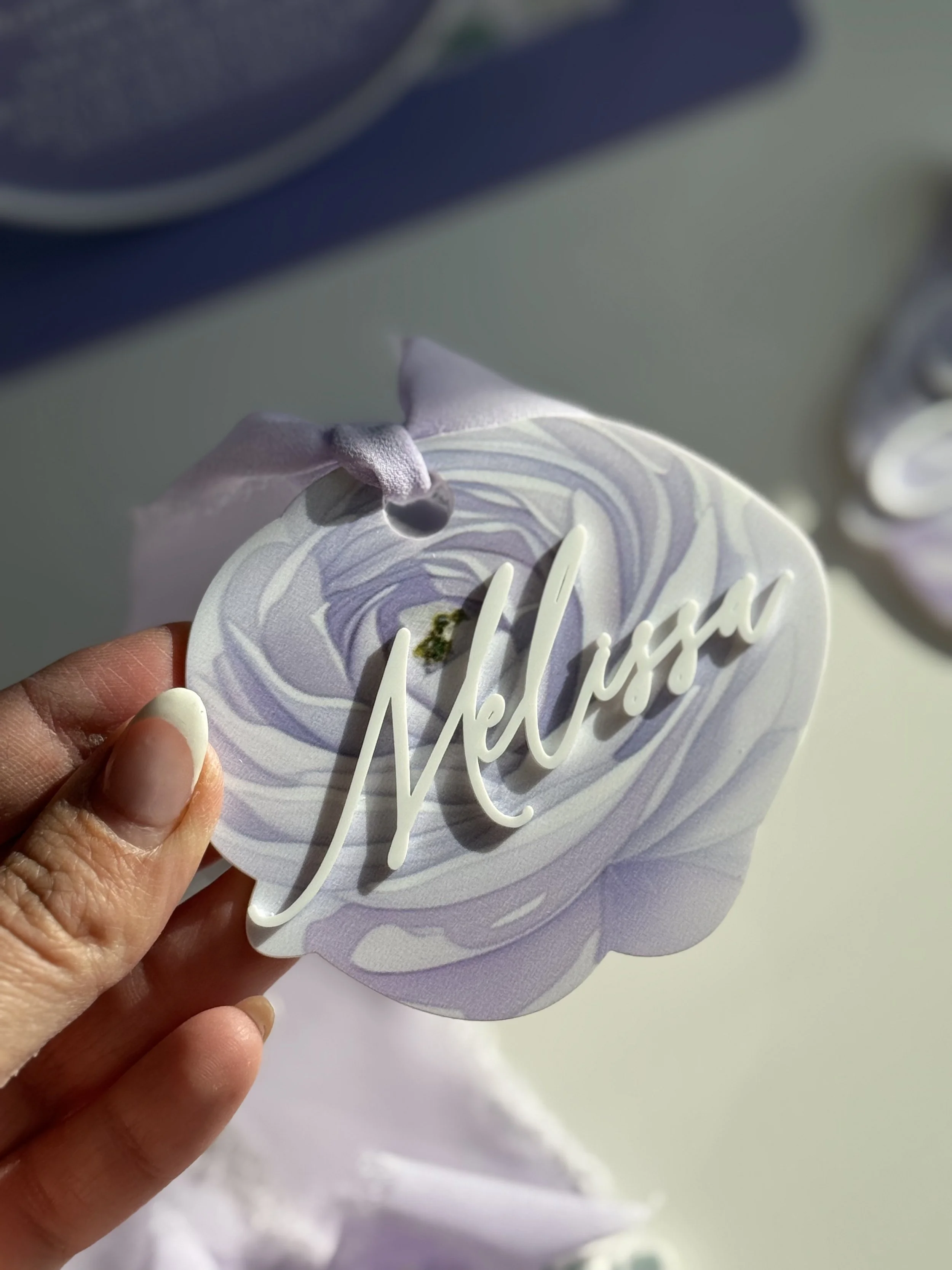 A decorative piece with the word 'Nellisa' in cursive, on a lavender and white marbled background, topped with lavender-colored fabric ribbon.