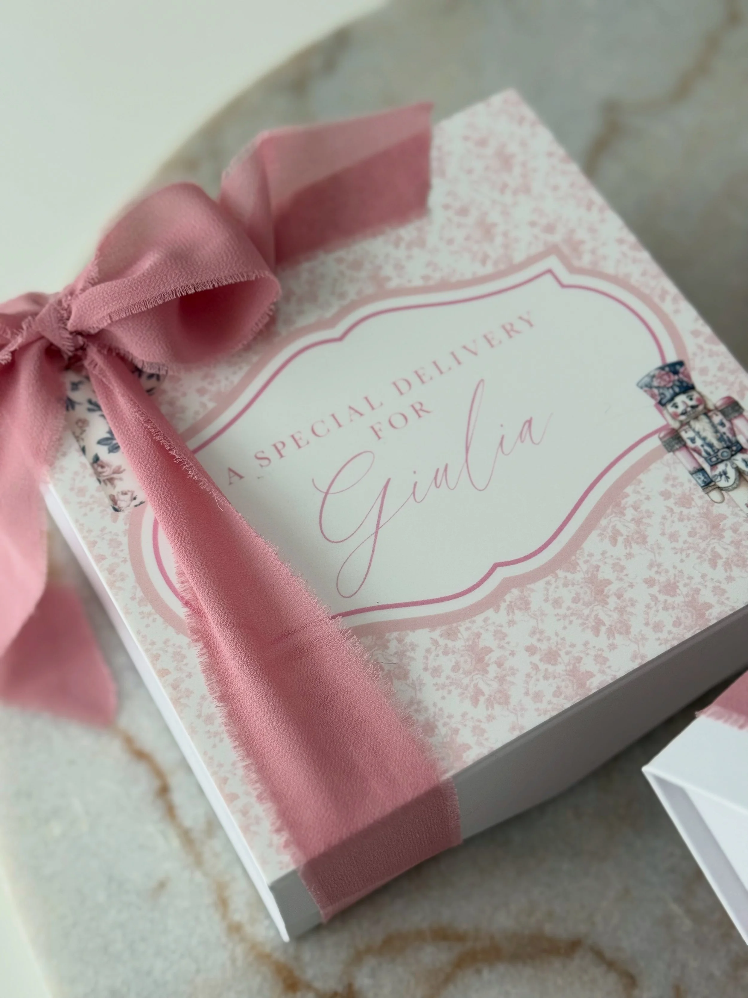 A decorative pink gift box with a pink ribbon, labeled 'A special delivery for Gimal,' sitting on a marble surface.