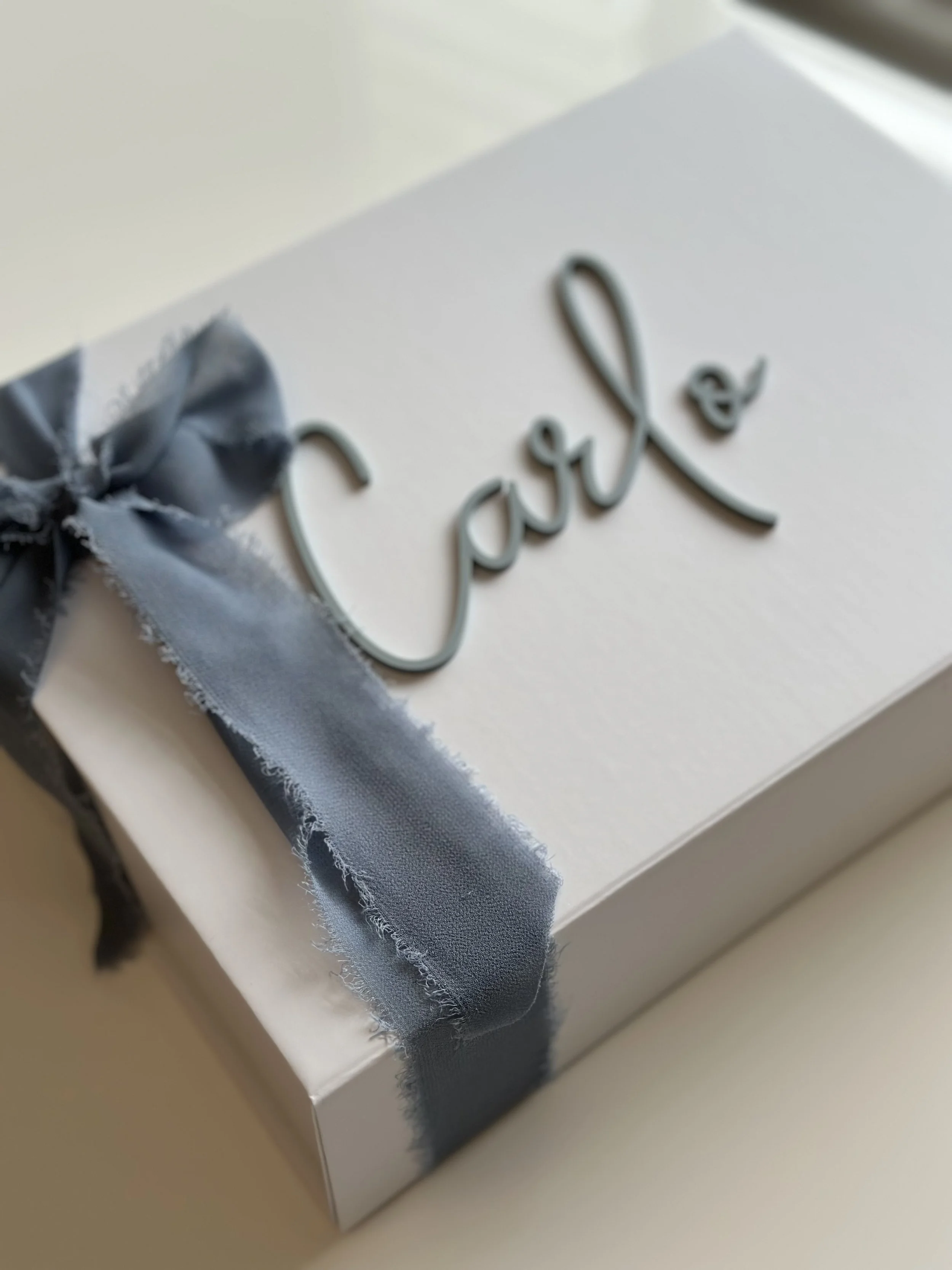 A white gift box decorated with a gray ribbon and bow, with the word 'love' written in metallic script on the top.