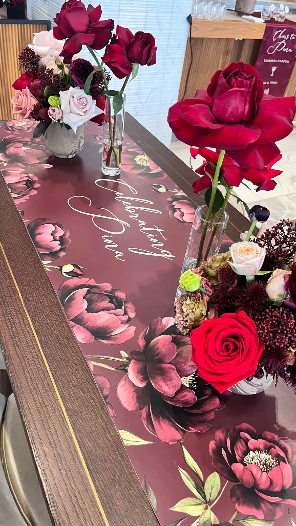 A table decorated with red and pink floral arrangements and a table runner that reads "Breakfast and Fiance" with a floral design.