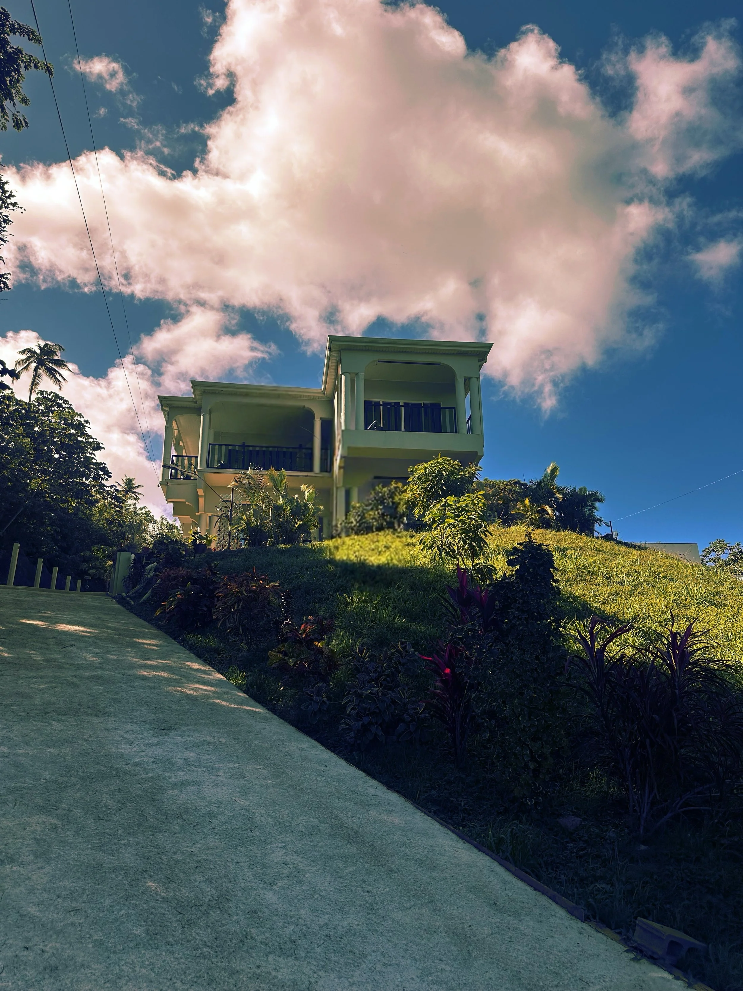 Exterior view of Haven Hill Guesthouse in Tobago, a hillside home surrounded by lush greenery under a blue sky with soft clouds