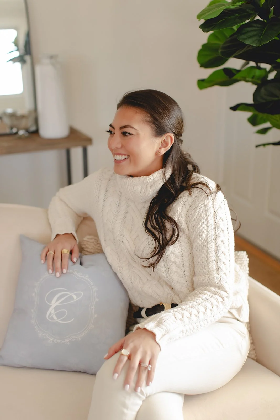 Business owner sitting on a couch in a cream sweater and jeans smiling to the right in an office space