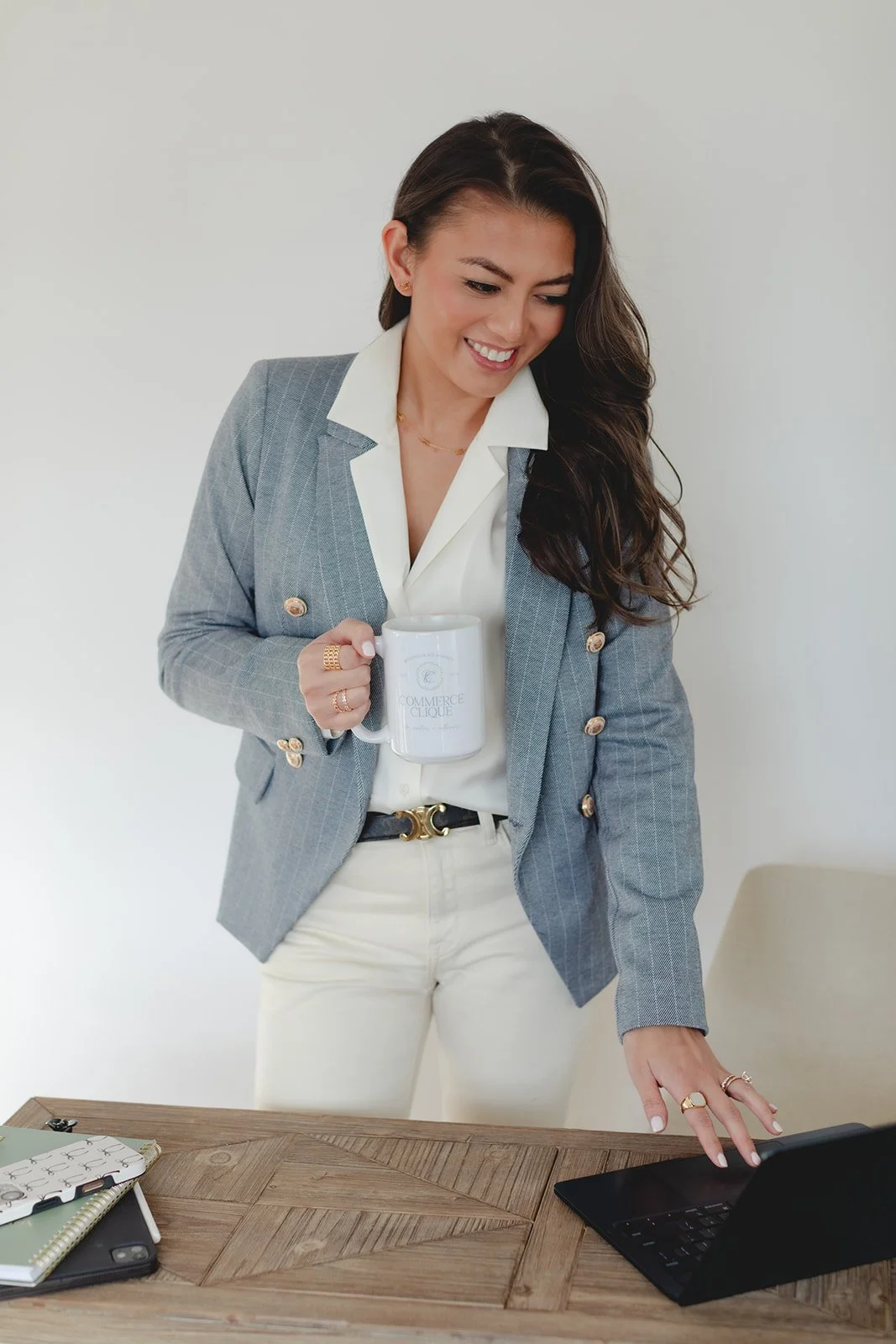 Business woman in a professional outfit standing behind a desk while on the computer and holding a mug