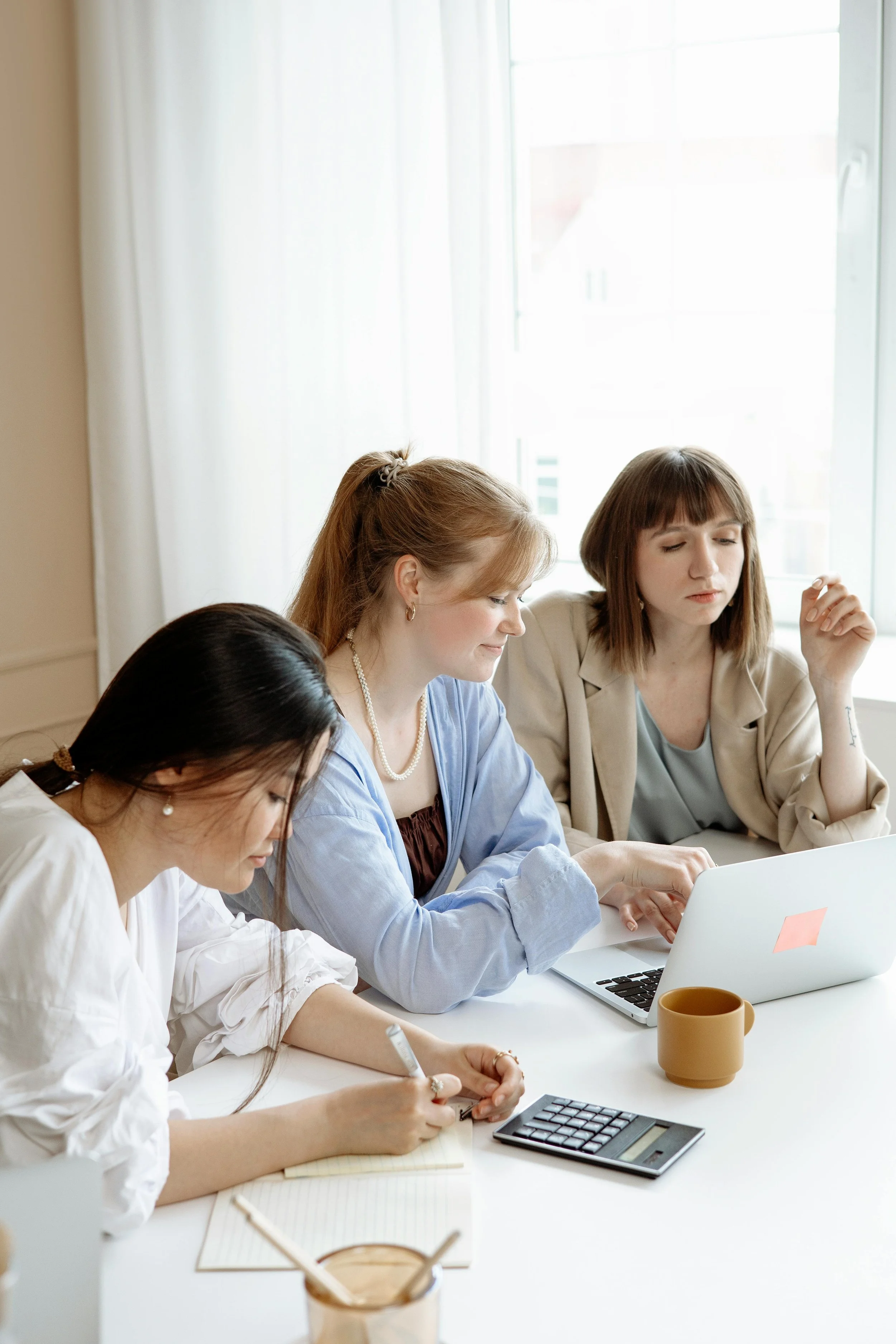 Team of women sitting at a desk with various office supplies working together