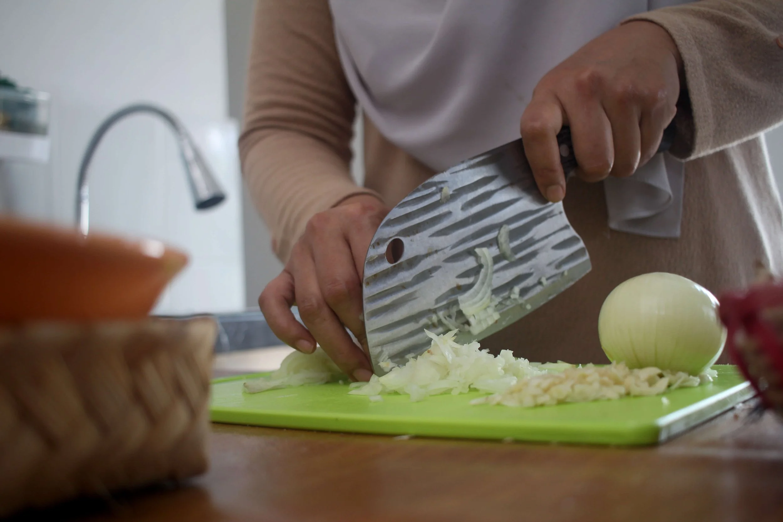Closeup of a Muslim Asian woman’s hand slicing an onion on a cutting board.