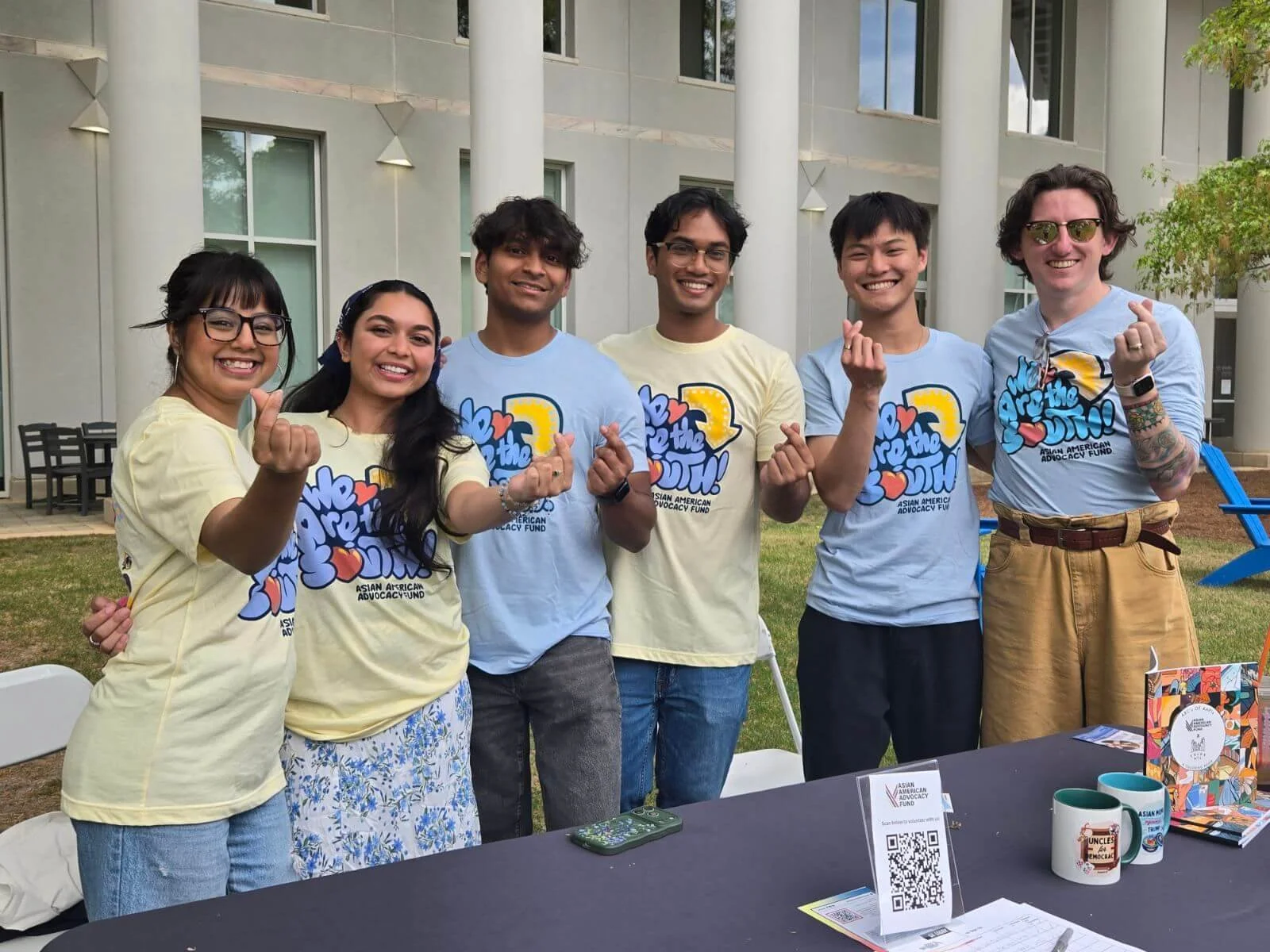 Staff and volunteers, posing and doing finger hearts, wearing matching shirts that say "we are the South" during a community event. 