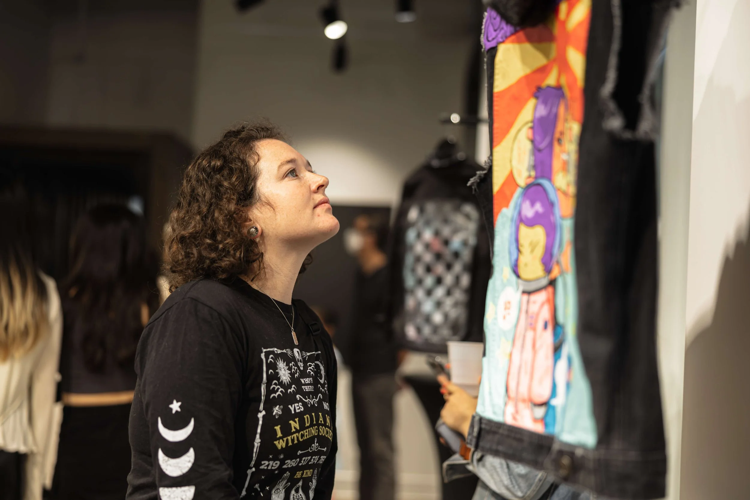 Community member viewing denim jacket with artwork created by artist Killamari during Threads of Justice opening reception.