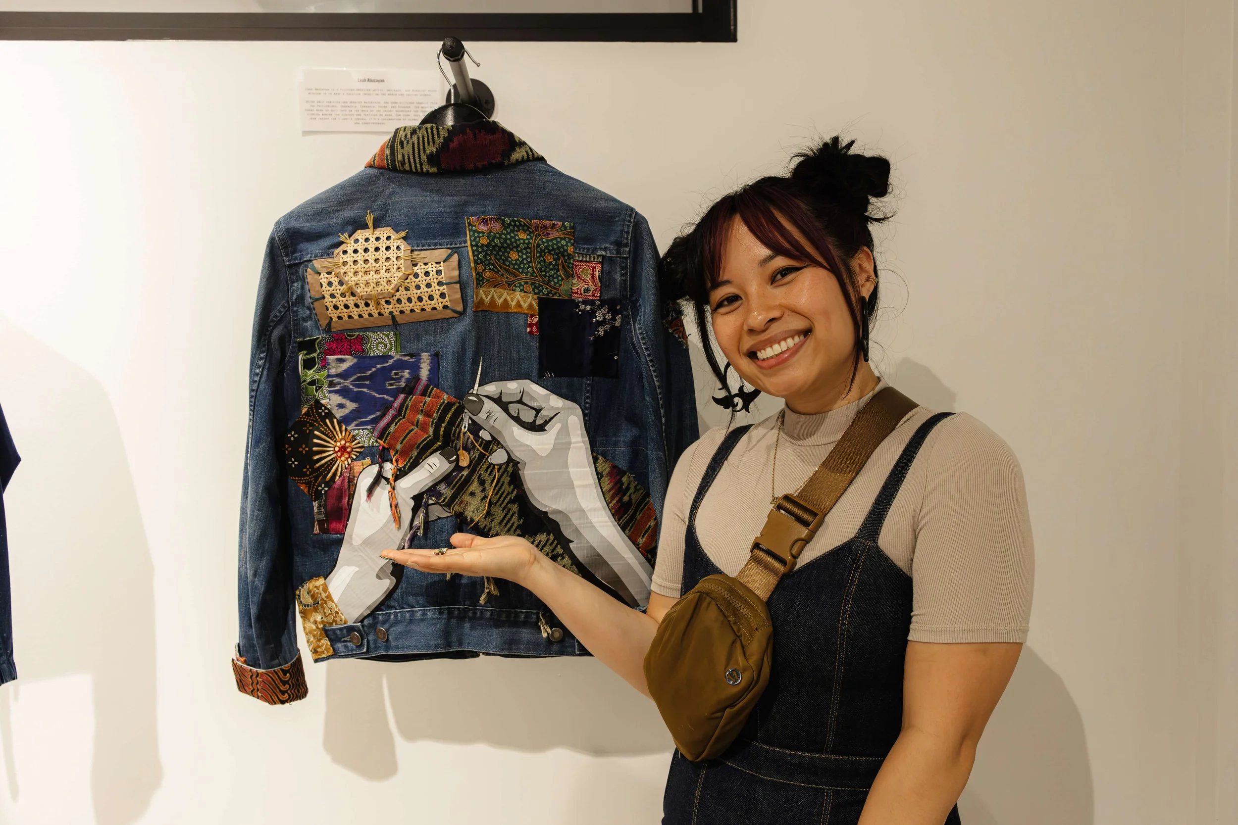 Artist HellaLeah stands in front of her art piece displayed on a denim jacket at the Threads of Justice opening reception.