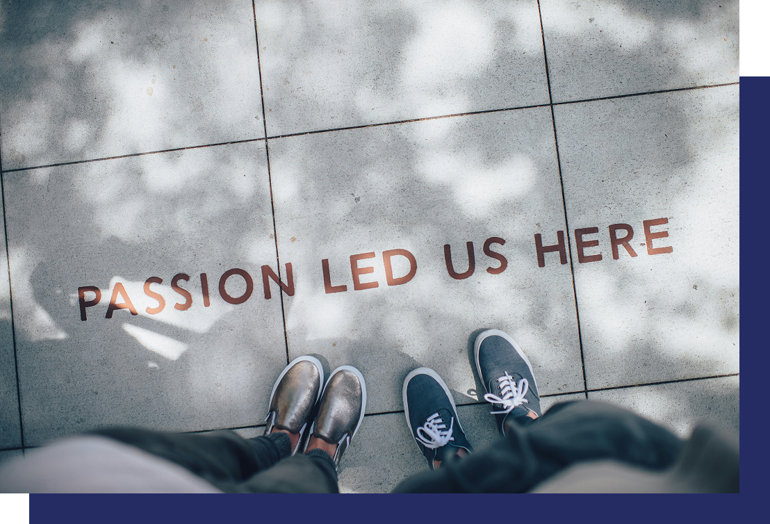 View of two pairs of shoes standing on pavement with the words "PASSION LED US HERE" written on the ground.