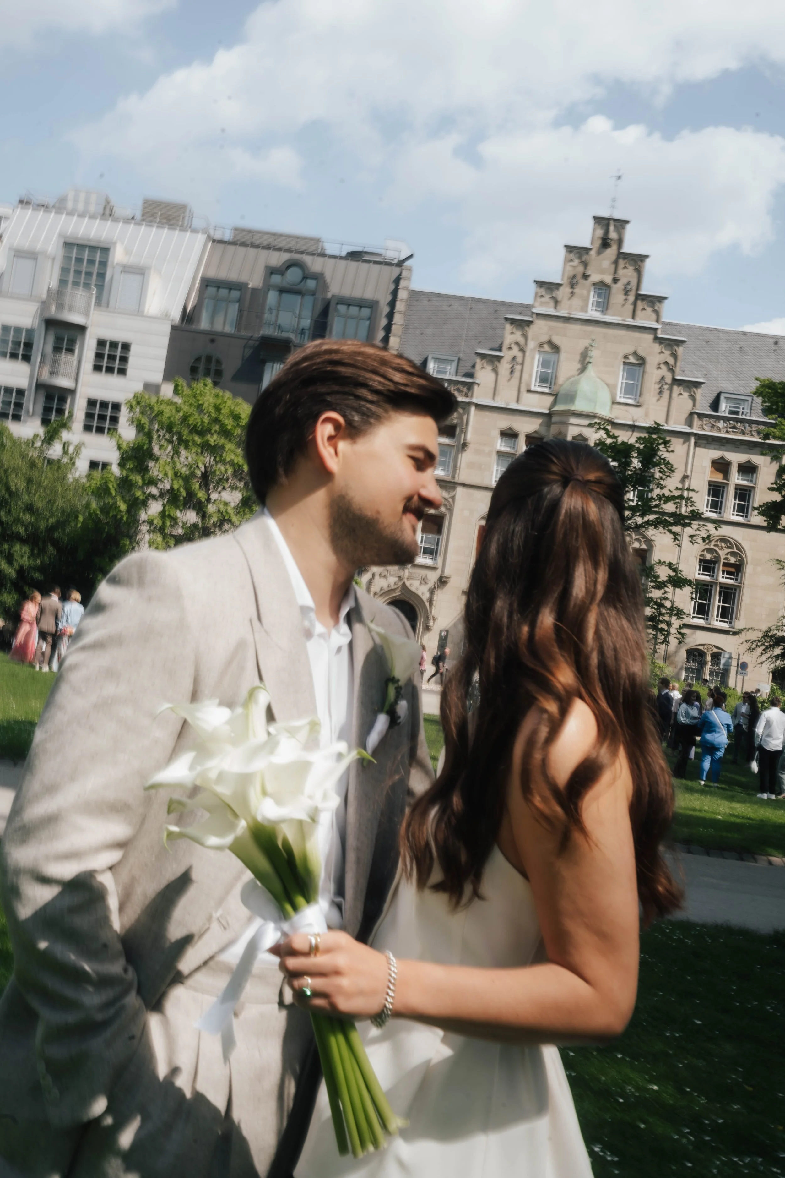Ein Mann und eine Frau bei einer Hochzeit im Freien, umgeben von Bäumen und historischen Gebäuden, die Happiness und Romantik zeigen.