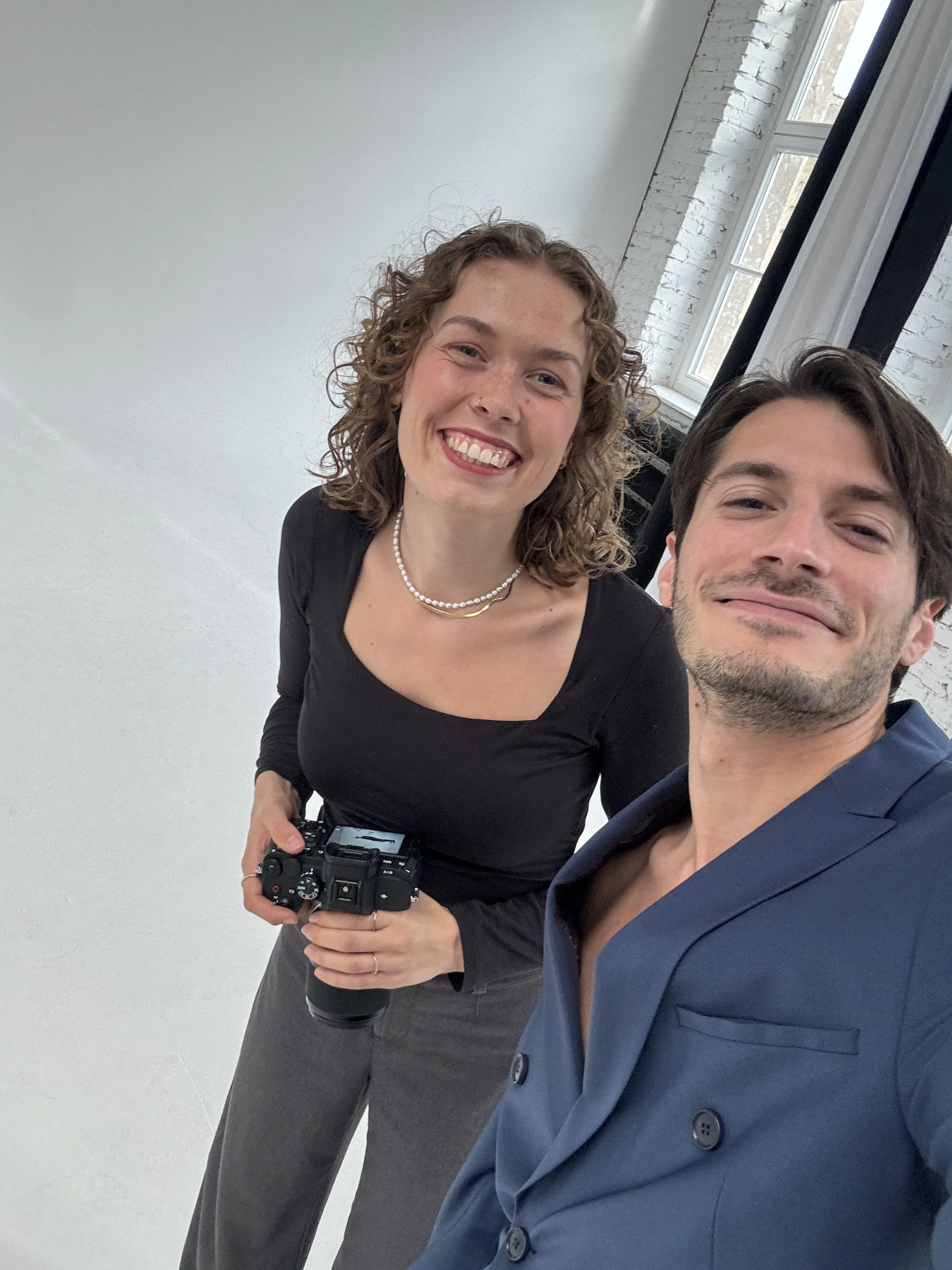 Zwei Menschen posieren für eine Selfie in einem modernen Raum mit weißen Wänden und großen Fenstern, die Licht hereinlassen.