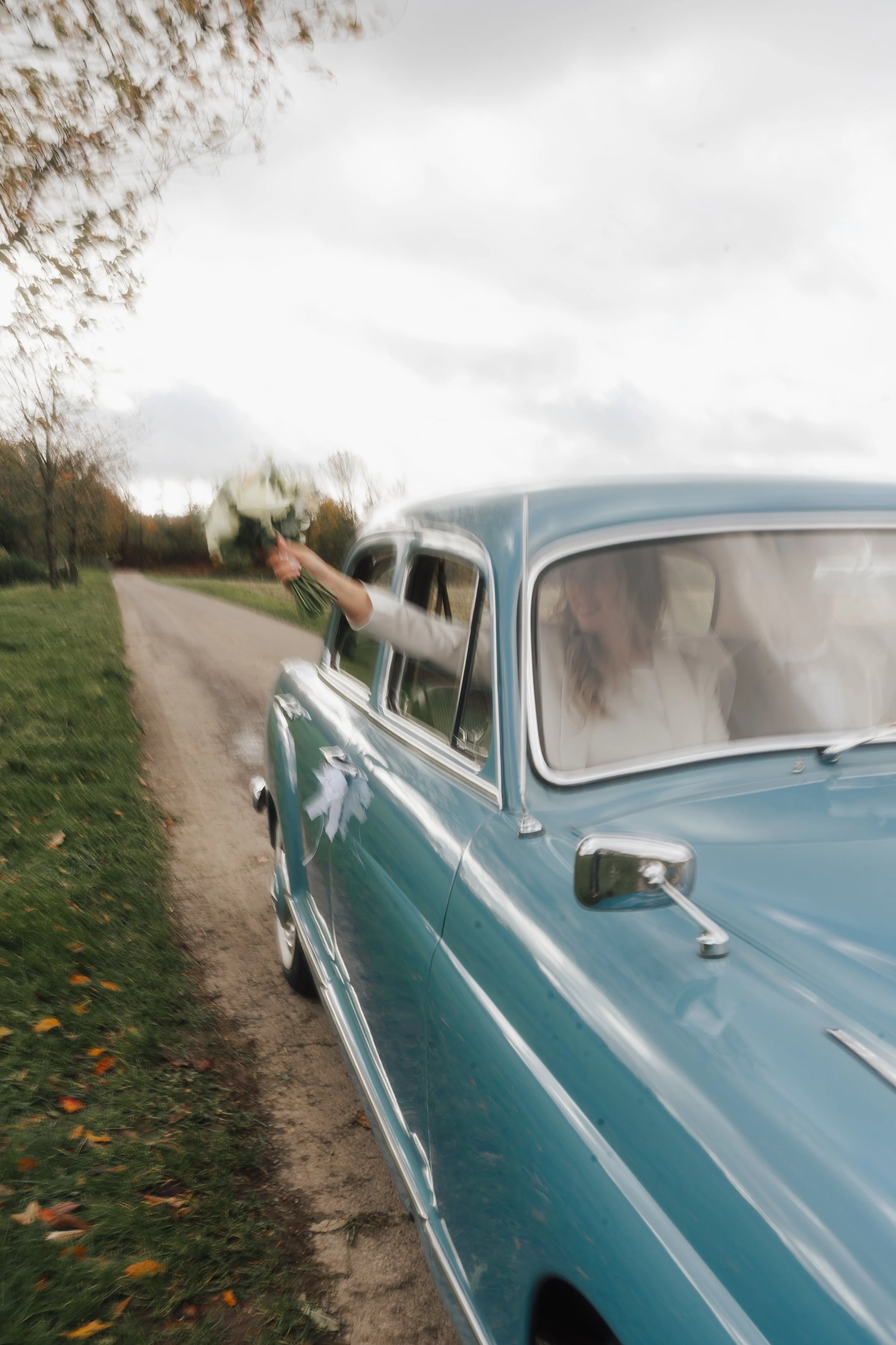 Hochzeitstag, Hochzeitsauto und die Braut hält den Brautstrauß aus dem fahrenden Auto