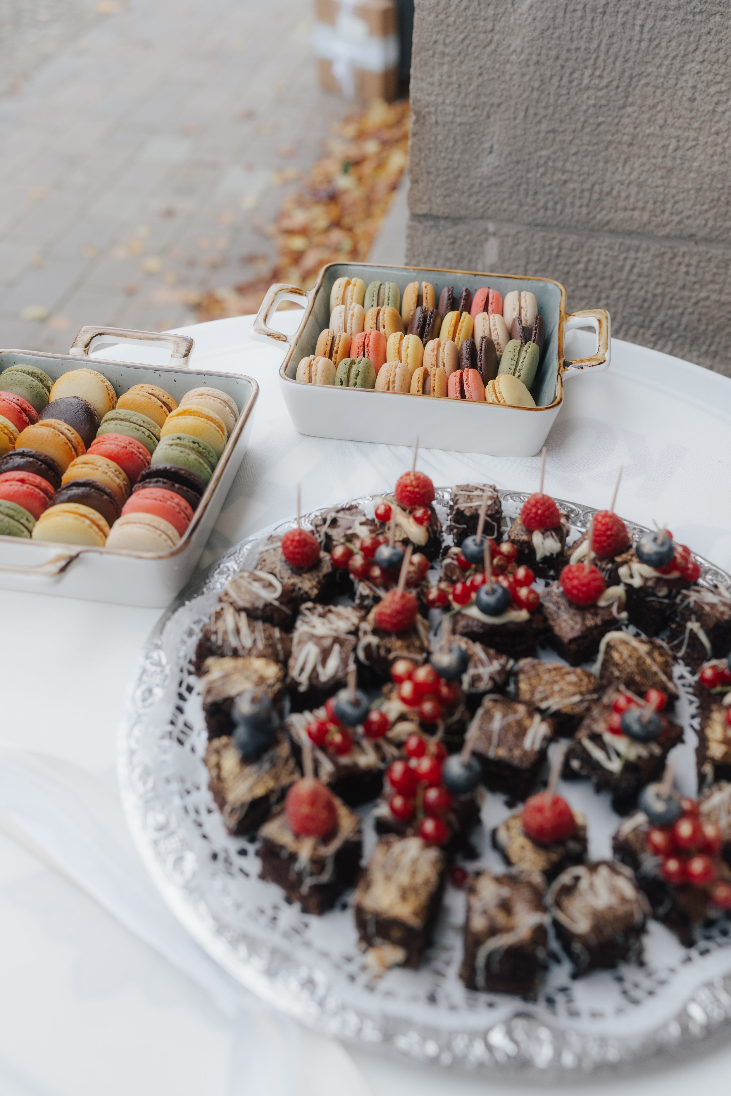 Bunte Macarons auf einem weißen Tablett bei einer Feier, im Hintergrund ein Kuchen mit Beeren.