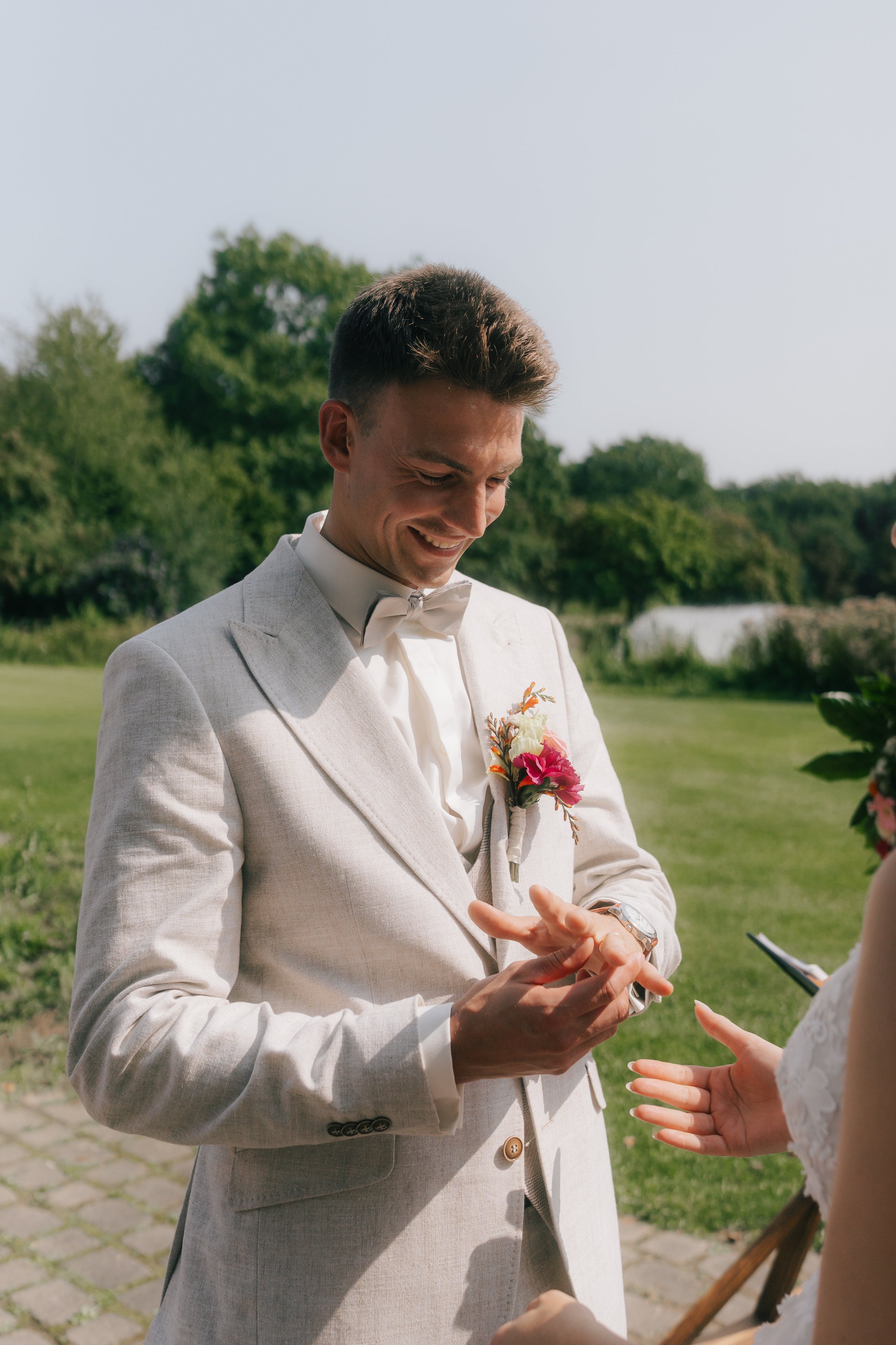 Ein glücklicher Bräutigam in Weiß bei einer Trauung im Freien beim Austausch der Ringe.