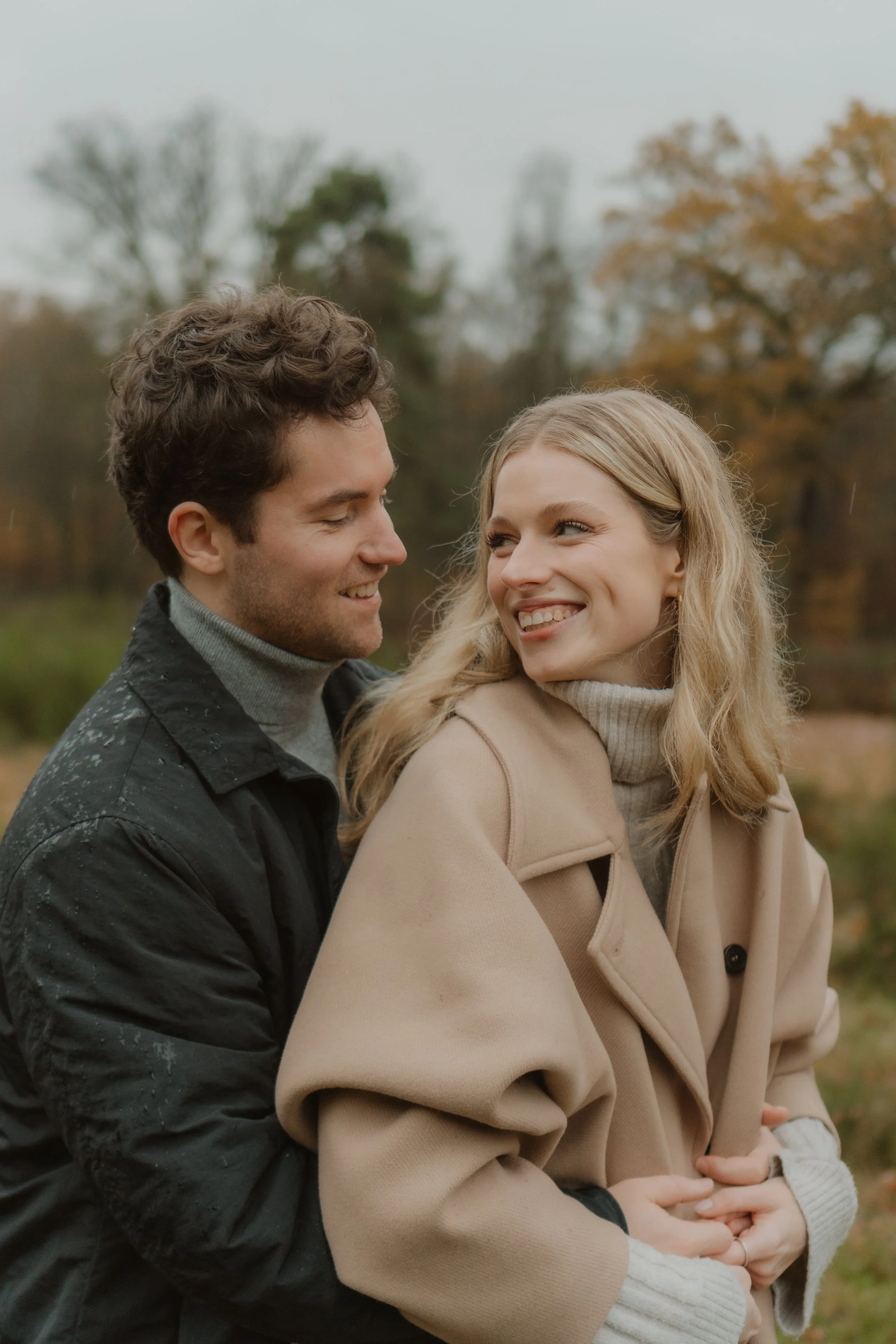 Ein Paar bei ihrem modernen Paarshooting in Köln im Herbst in einer Natur mit Bäumen in der Nähe, das sich liebevoll ansieht.
