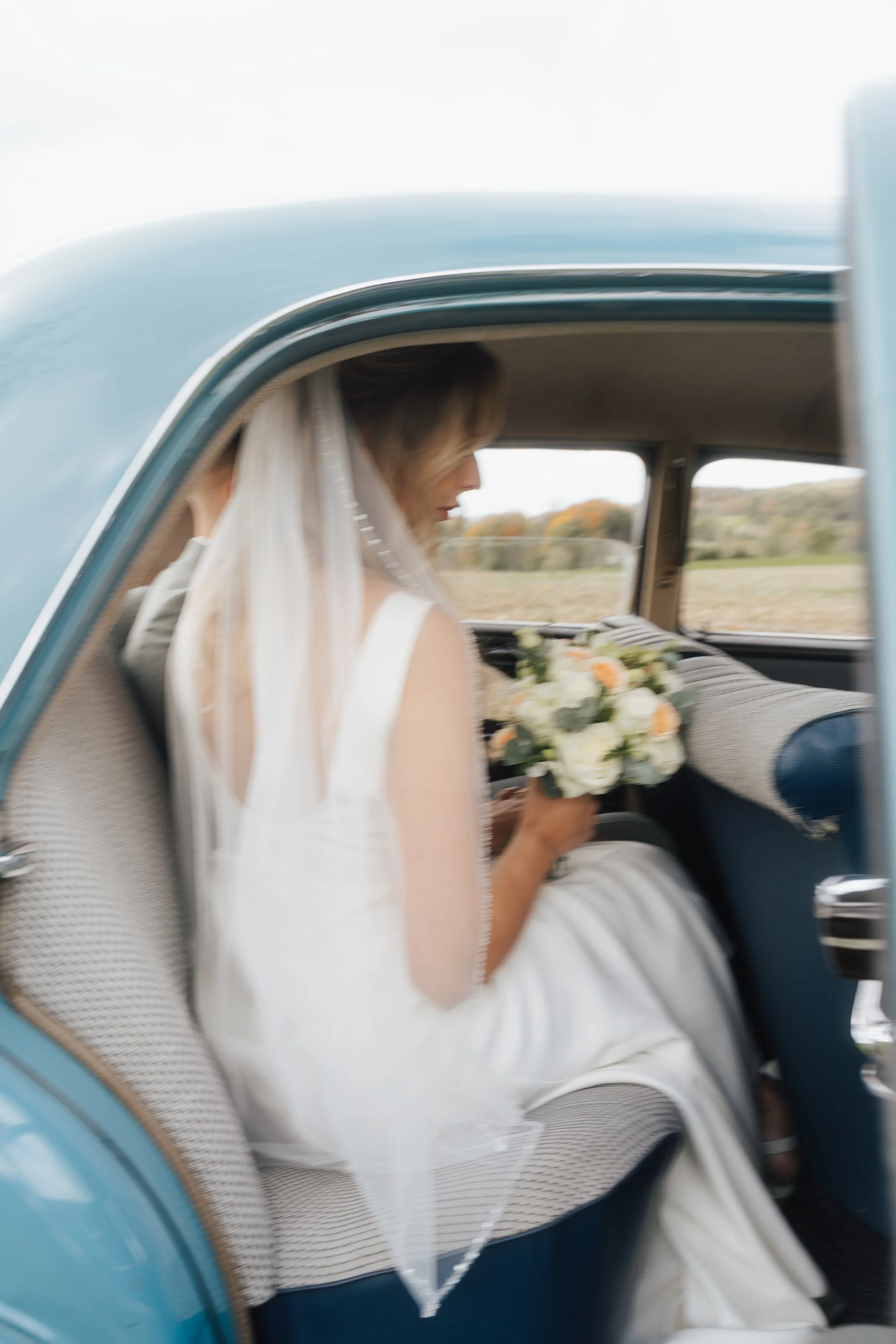 Eine Braut mit Schleier, die in einem Vintage-Auto sitzt, das mit Blumen dekoriert ist, im Freien auf dem Land.