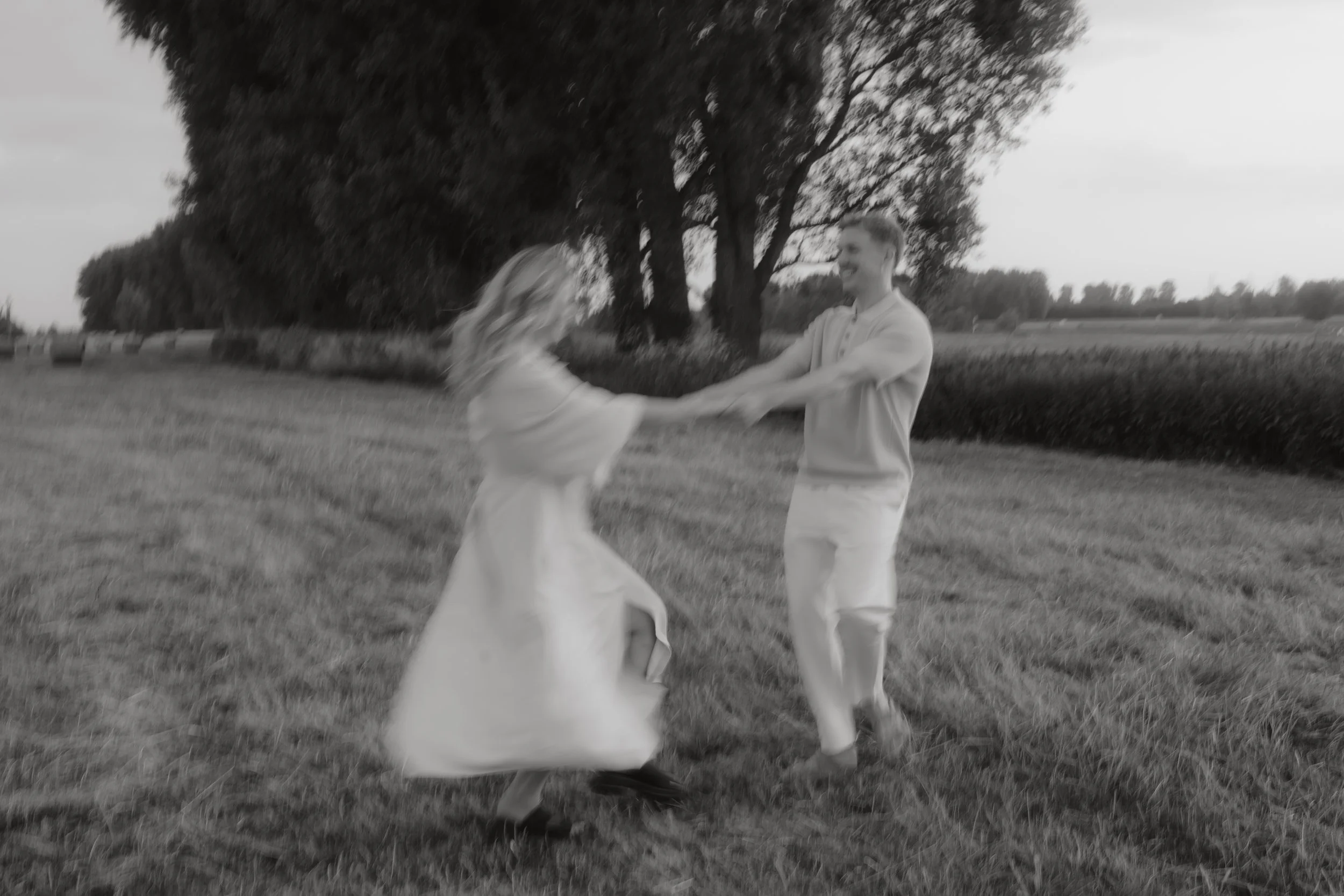 Ein Paar tanzt im Freien auf einer Wiese, umgeben von Bäumen, bei Sonnenuntergang, im Schwarz-Weiß-Stil.