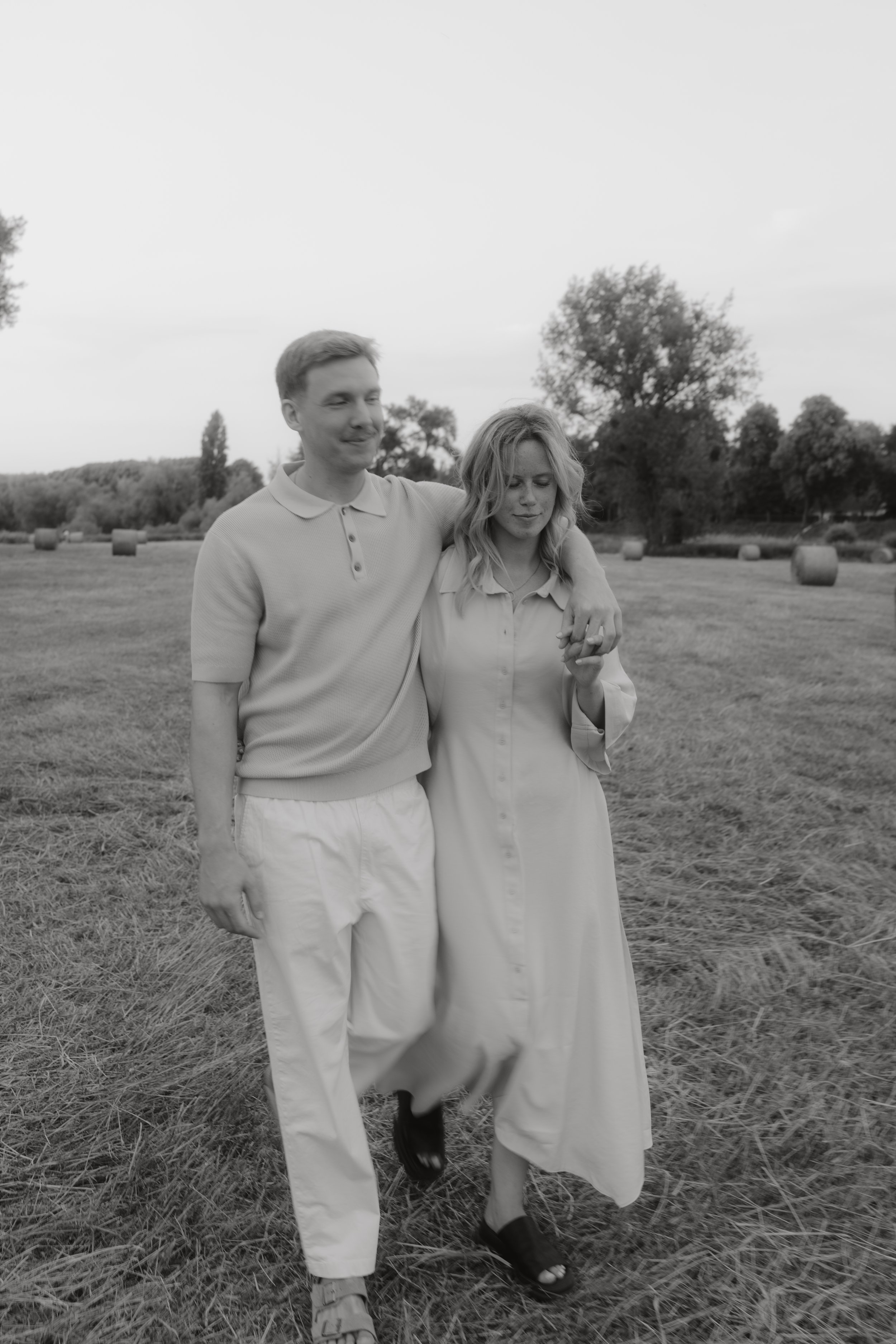 Ein Mann und eine Frau gehen gemeinsam durch eine offene Wiese. Der Mann hat den Arm um die Schulter der Frau, die beide scheinen entspannt und glücklich zu sein.