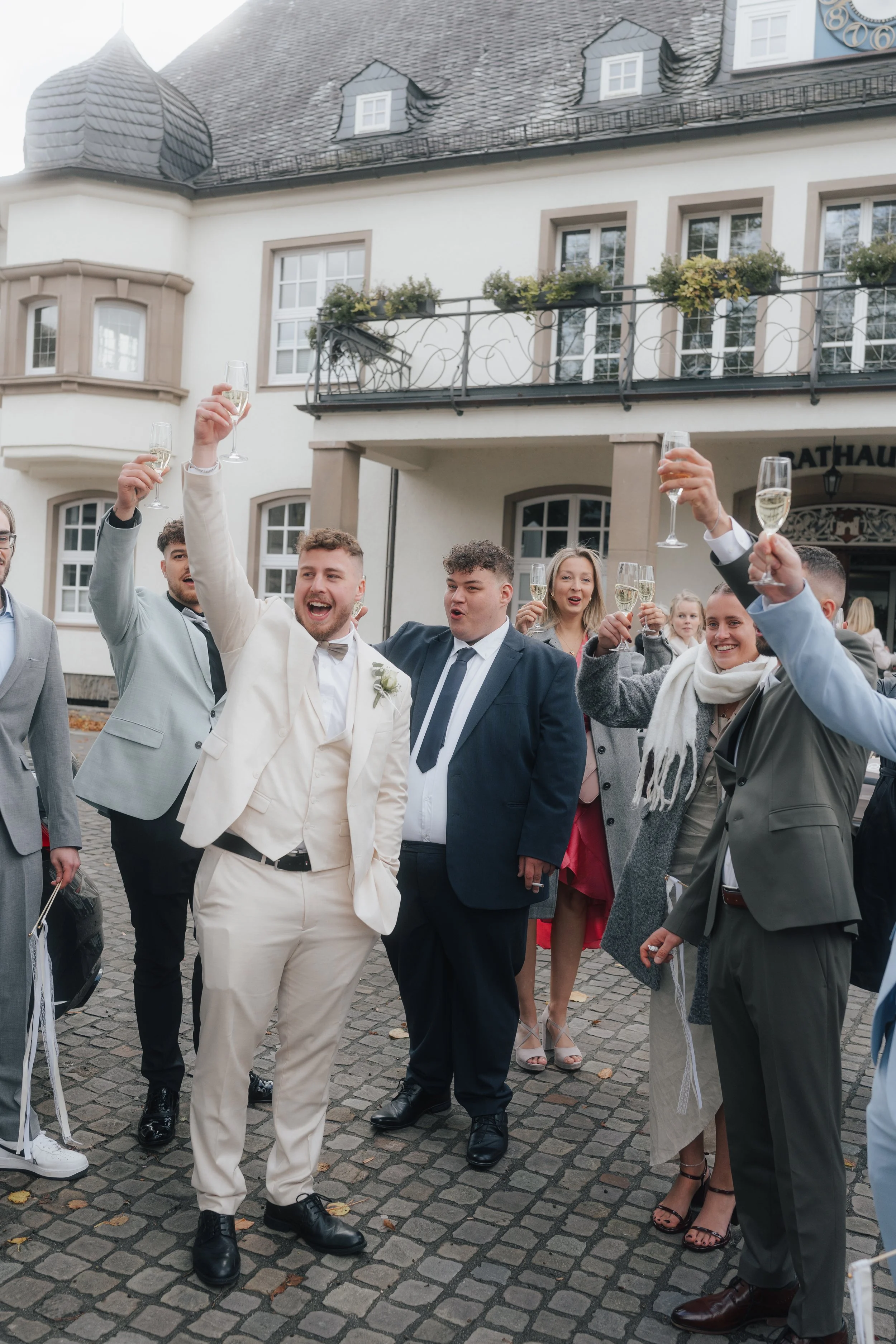 Menschen feiern mit Champagner in der Hand vor einem historischen Gebäude, vermutlich bei einer Hochzeit oder einem festlichen Anlass.