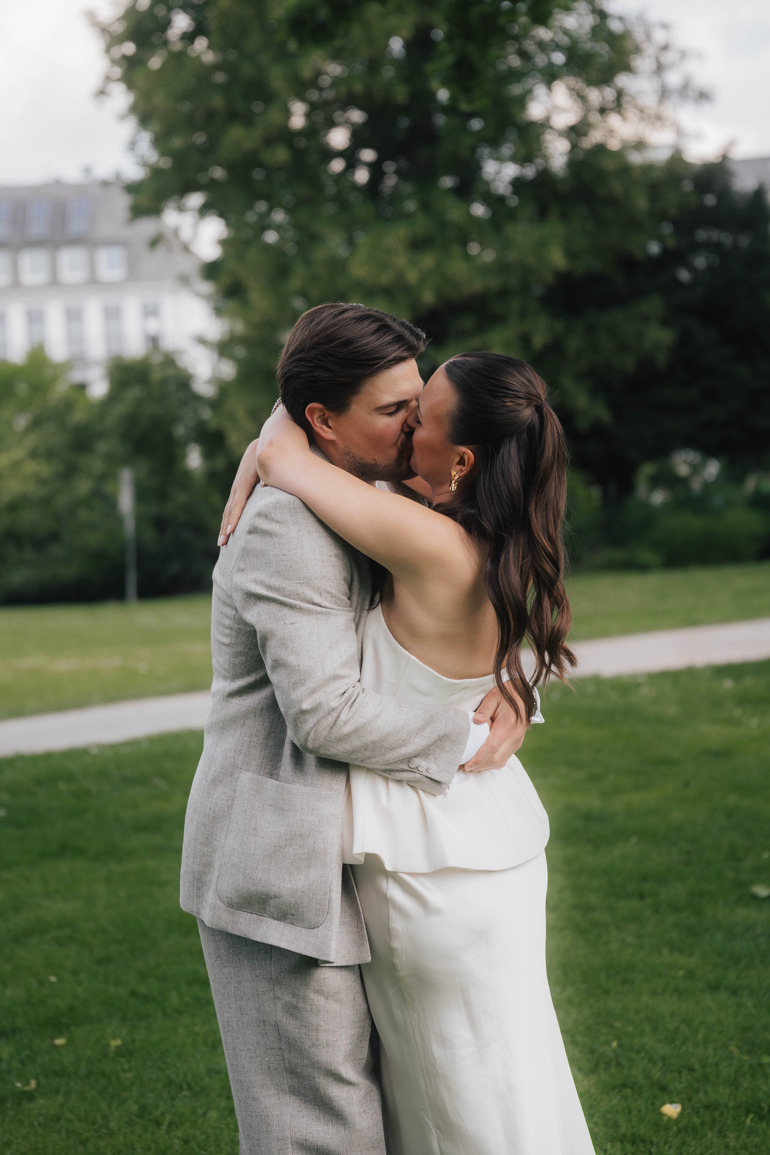 Ein Paar in Hochzeitskleidung küsst sich im Park unter einem großen Baum.