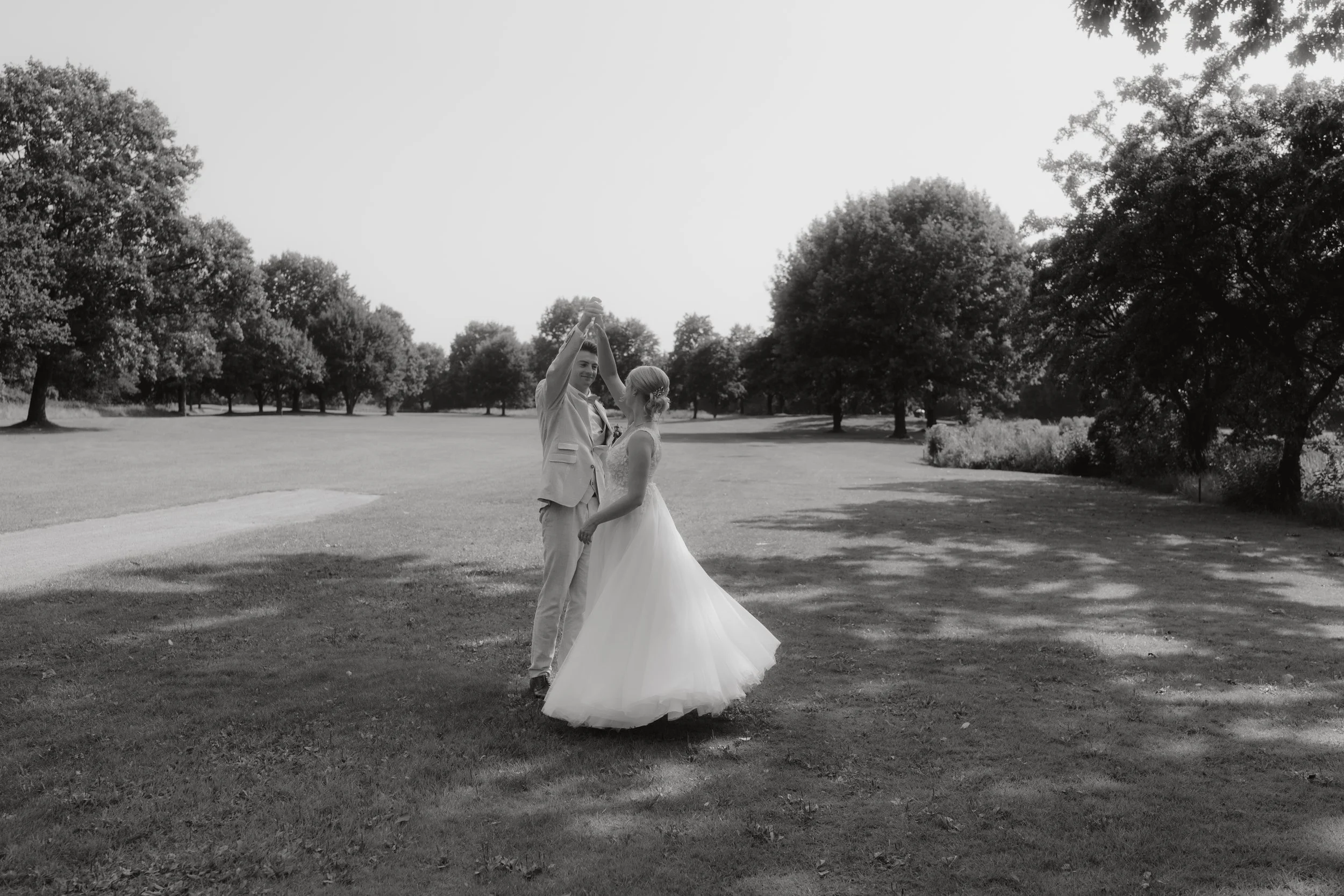 Ein Brautpaar tanzt im Park, umgeben von Bäumen, in Schwarz-Weiß-Fotografie.