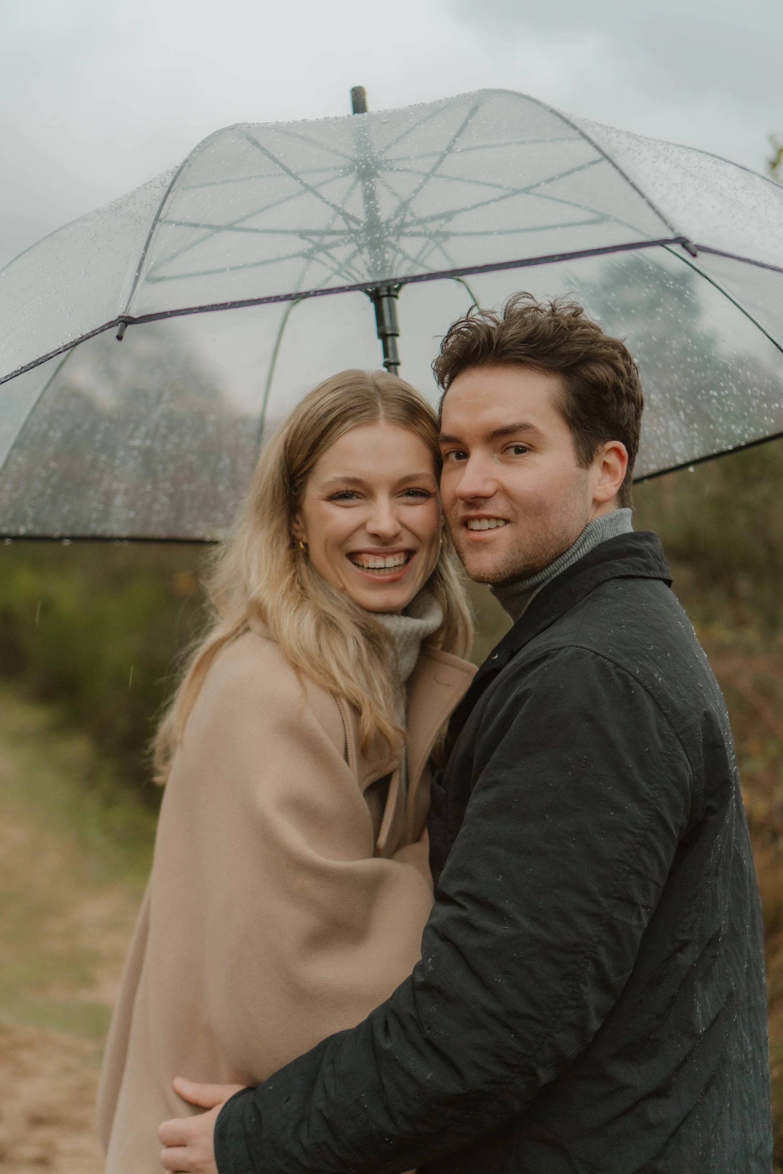 Ein lachendes Paar unter einem transparenten Regenschirm im Regen, umgeben von Natur