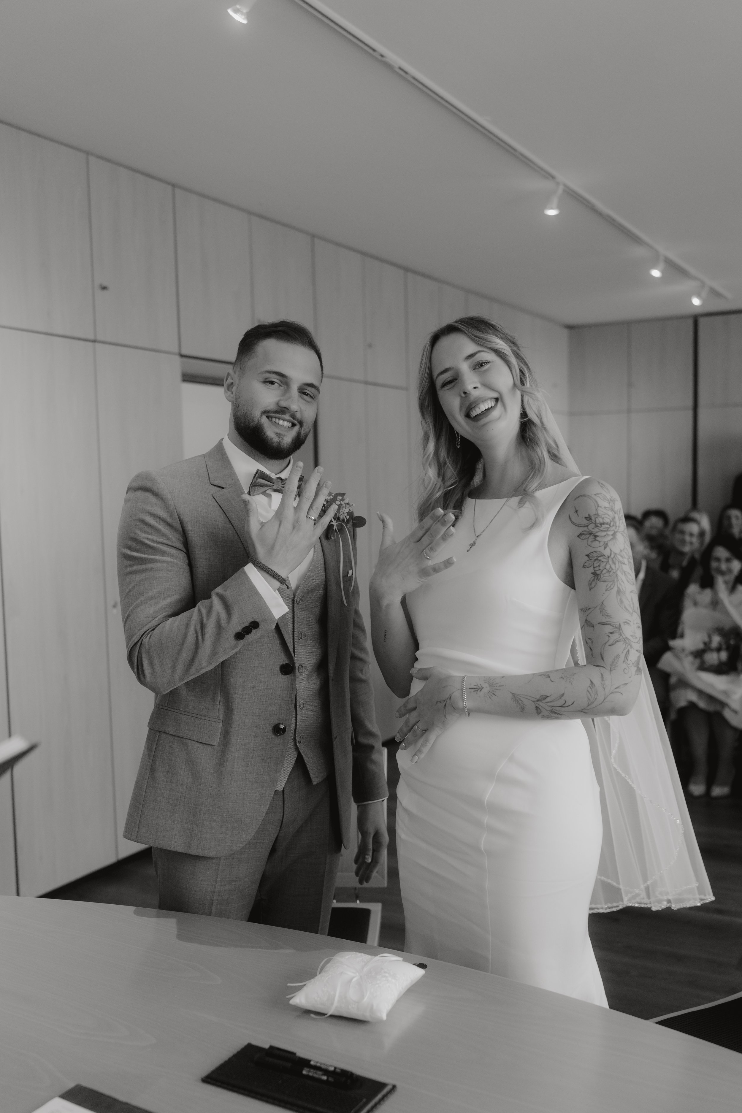 Ein Paar bei ihrer Trauung zeigt ihre Eheringe, Frauen in einem Brautkleid, Männer in einem Anzug, Hochzeitsgesellschaft ist glücklich