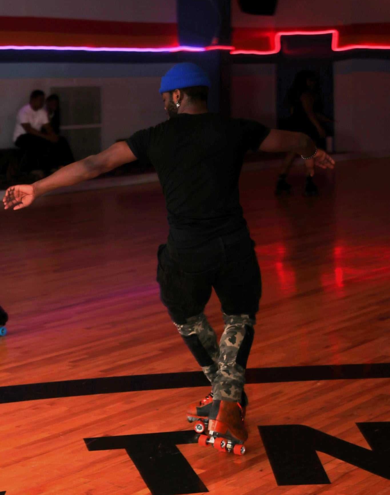Person roller skating on a wooden floor in a dimly lit roller rink with neon lights.