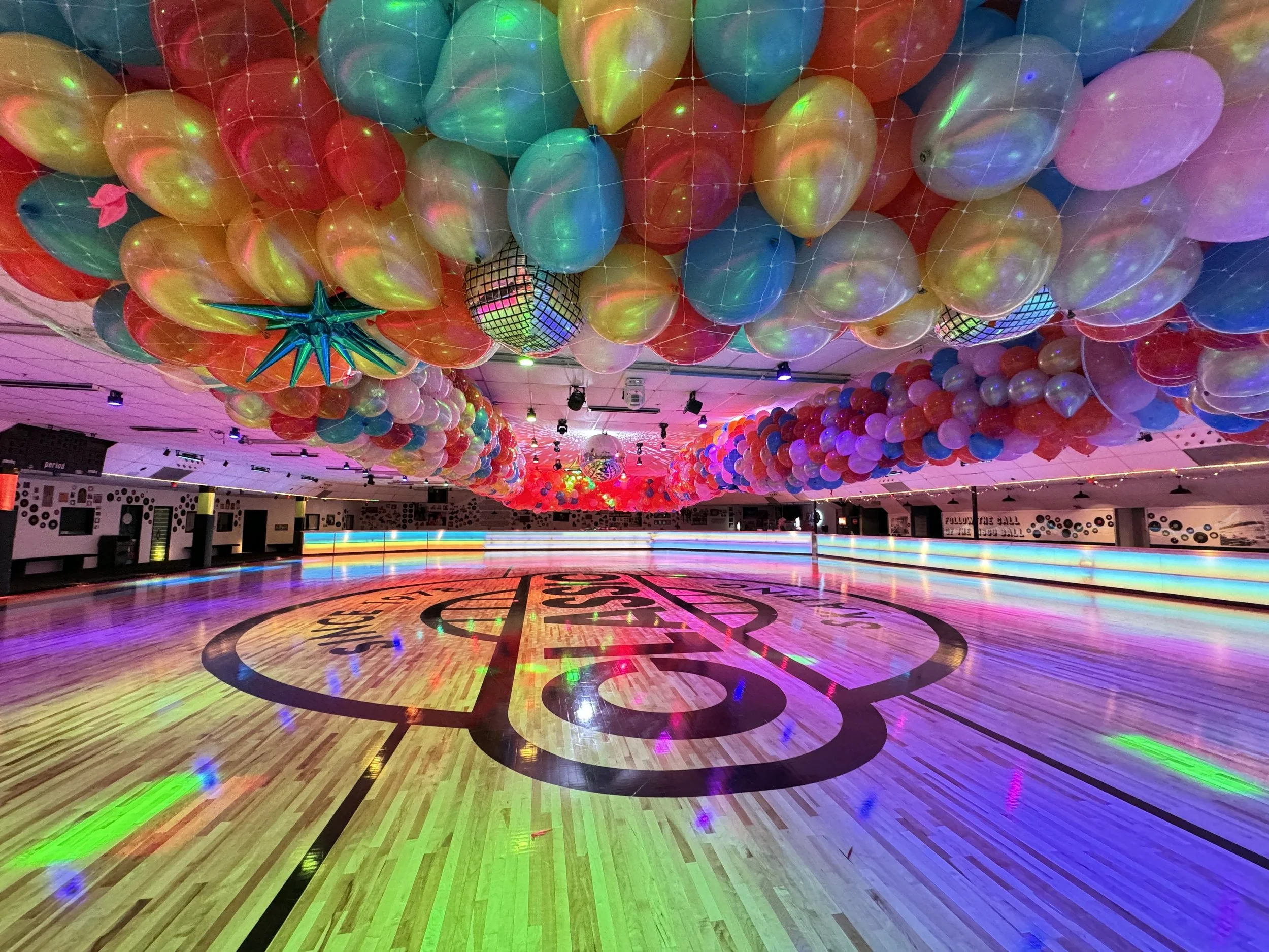 Empty indoor roller skating rink decorated with multi-colored balloons and lights.