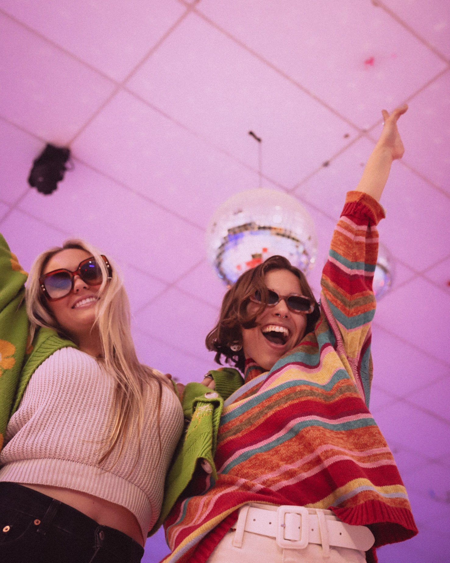 Two women dancing and smiling under disco balls with purple lighting.