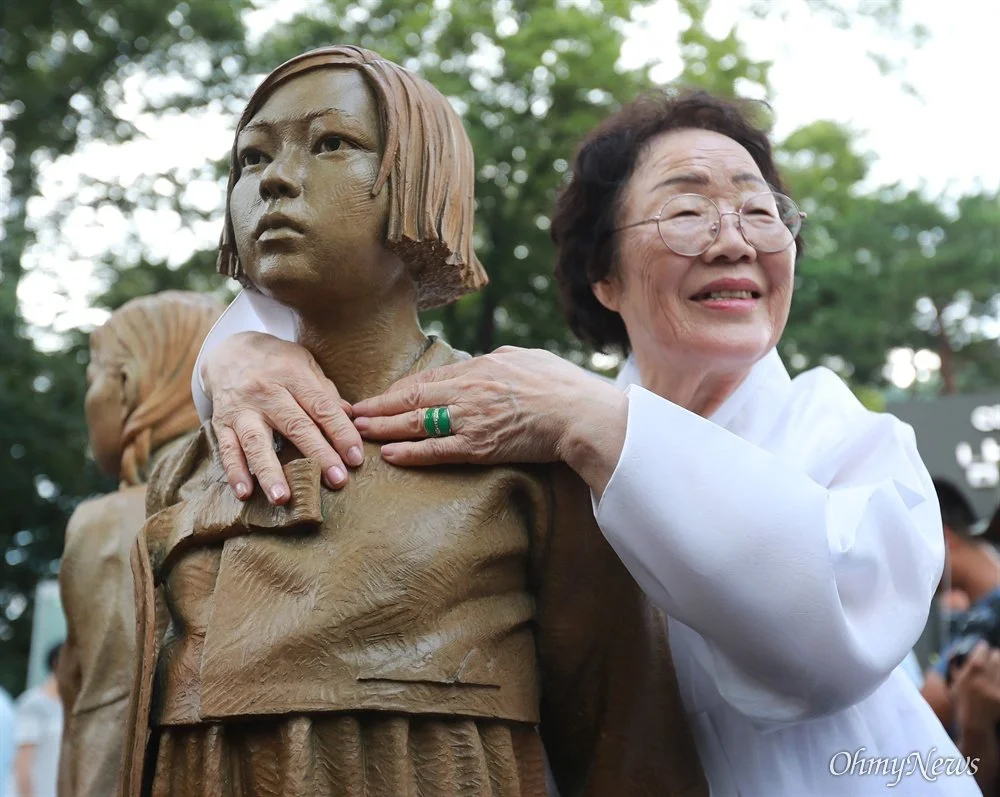 Lee Yong Soo, comfort woman survivor, standing with hand on shoulder of memorial statue honoring victims