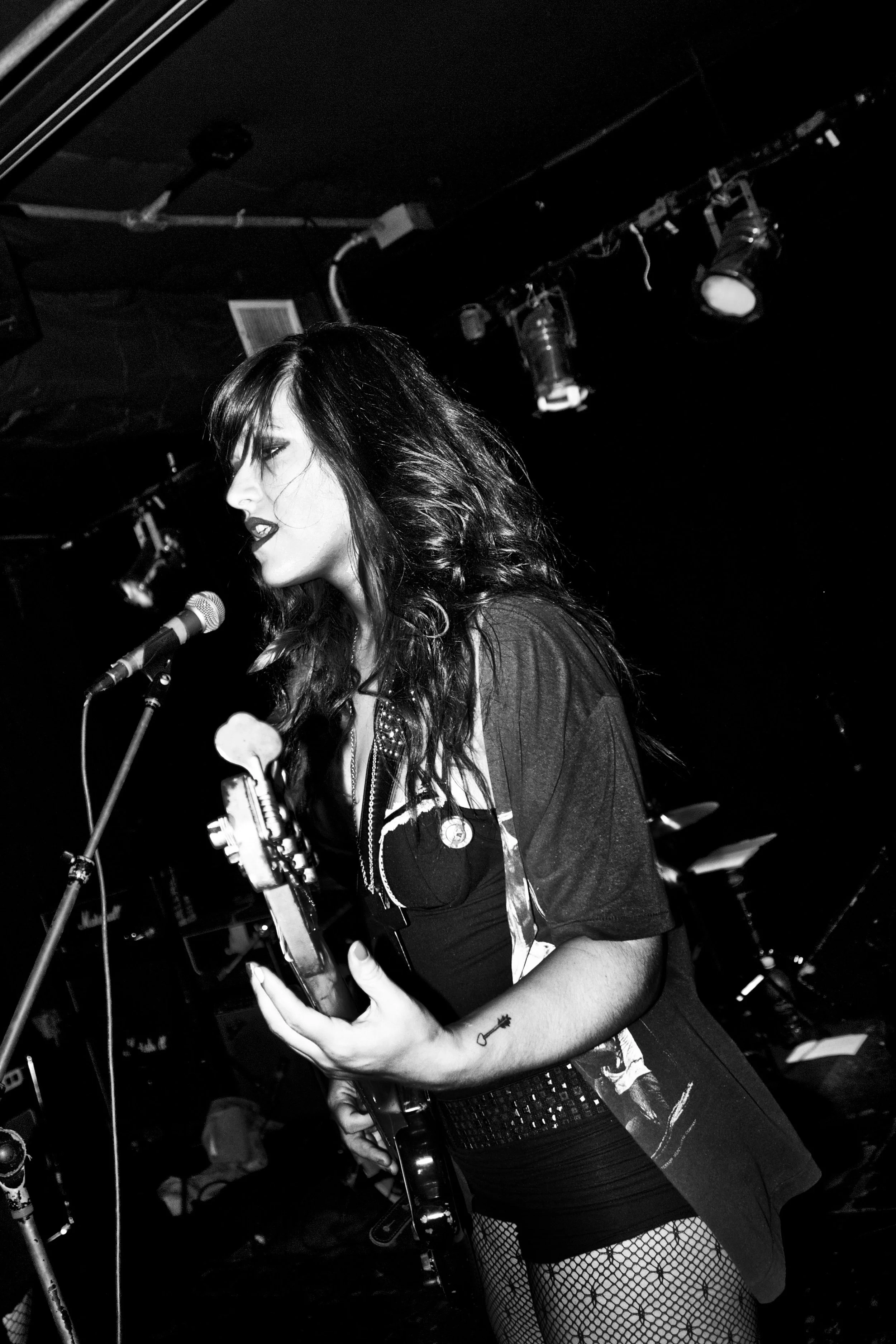 A female musician performs on stage with a guitar and a microphone, black and white photo, dark background, stage lights